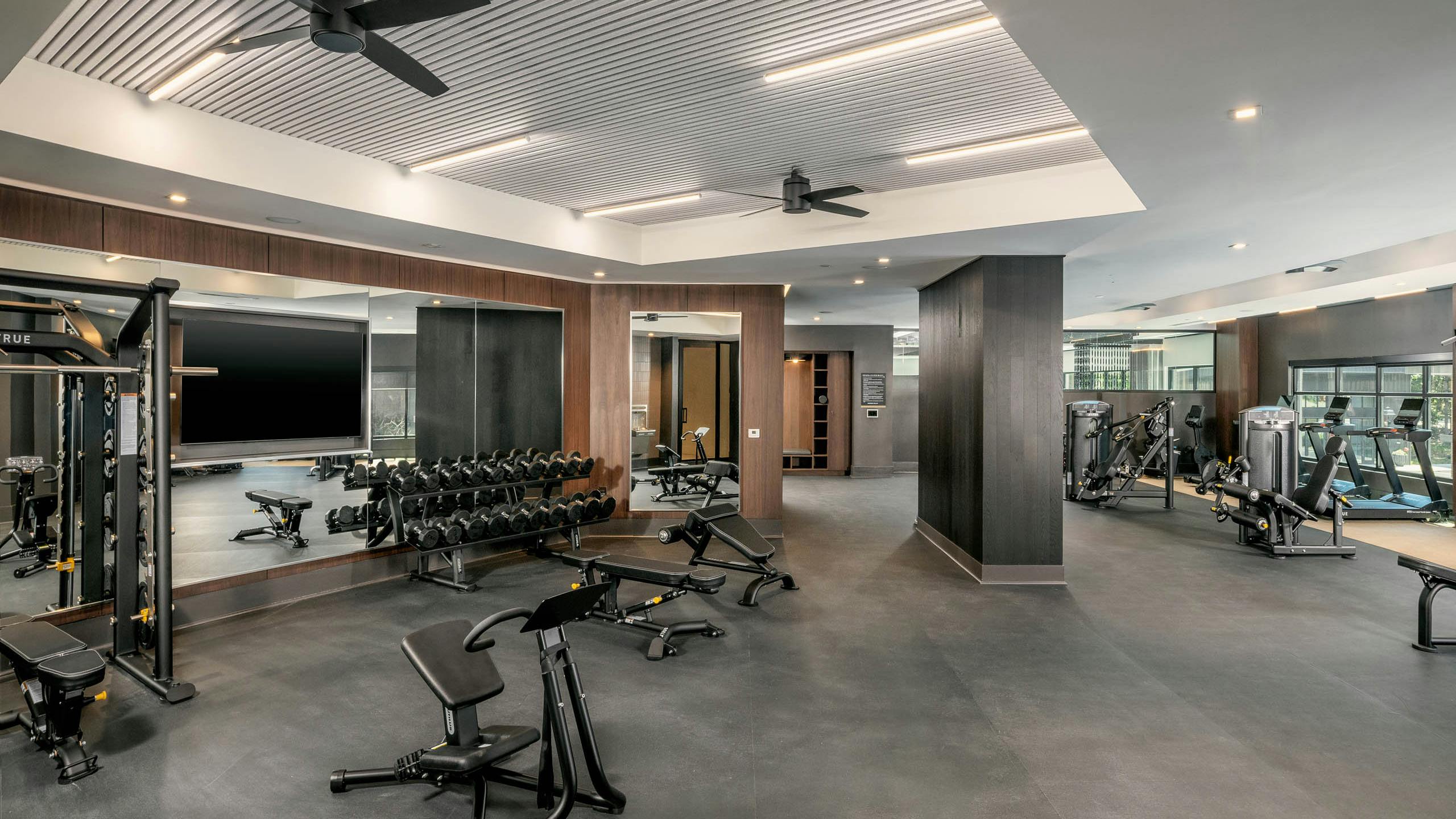 Spacious fitness center at AMLI Brookhaven apartments with a bench press and free weights and a full length mirror with ceiling fans