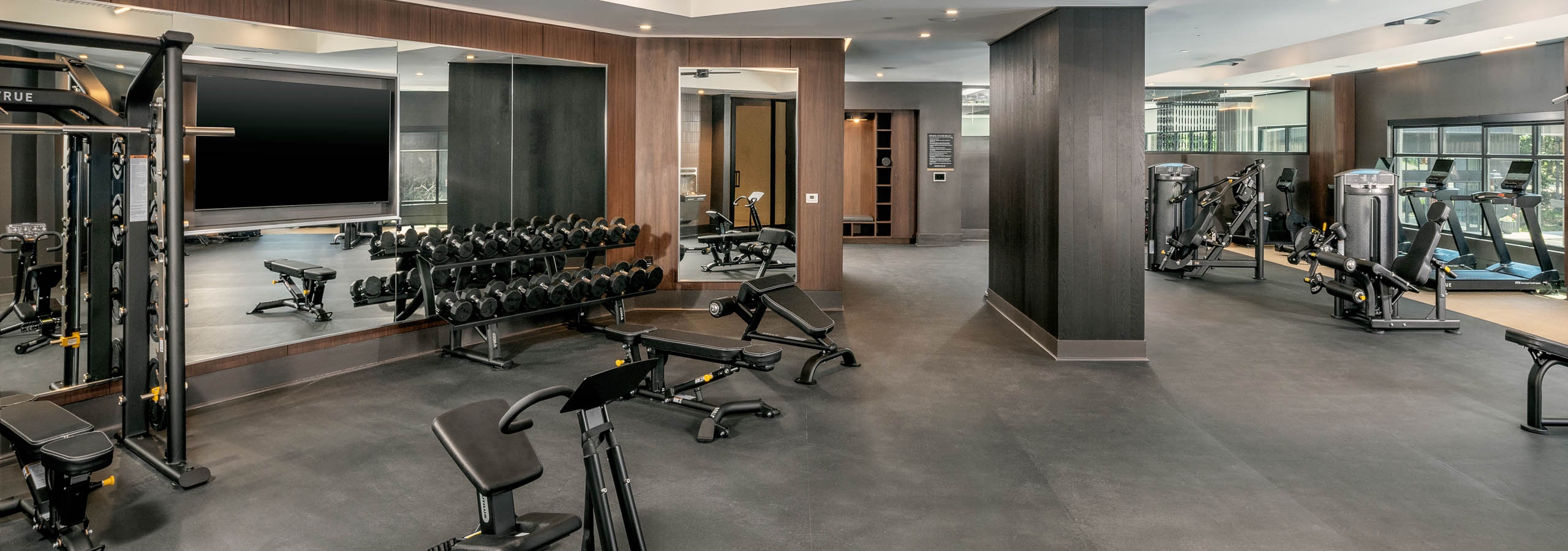 Spacious fitness center at AMLI Brookhaven apartments with a bench press and free weights and a full length mirror with ceiling fans