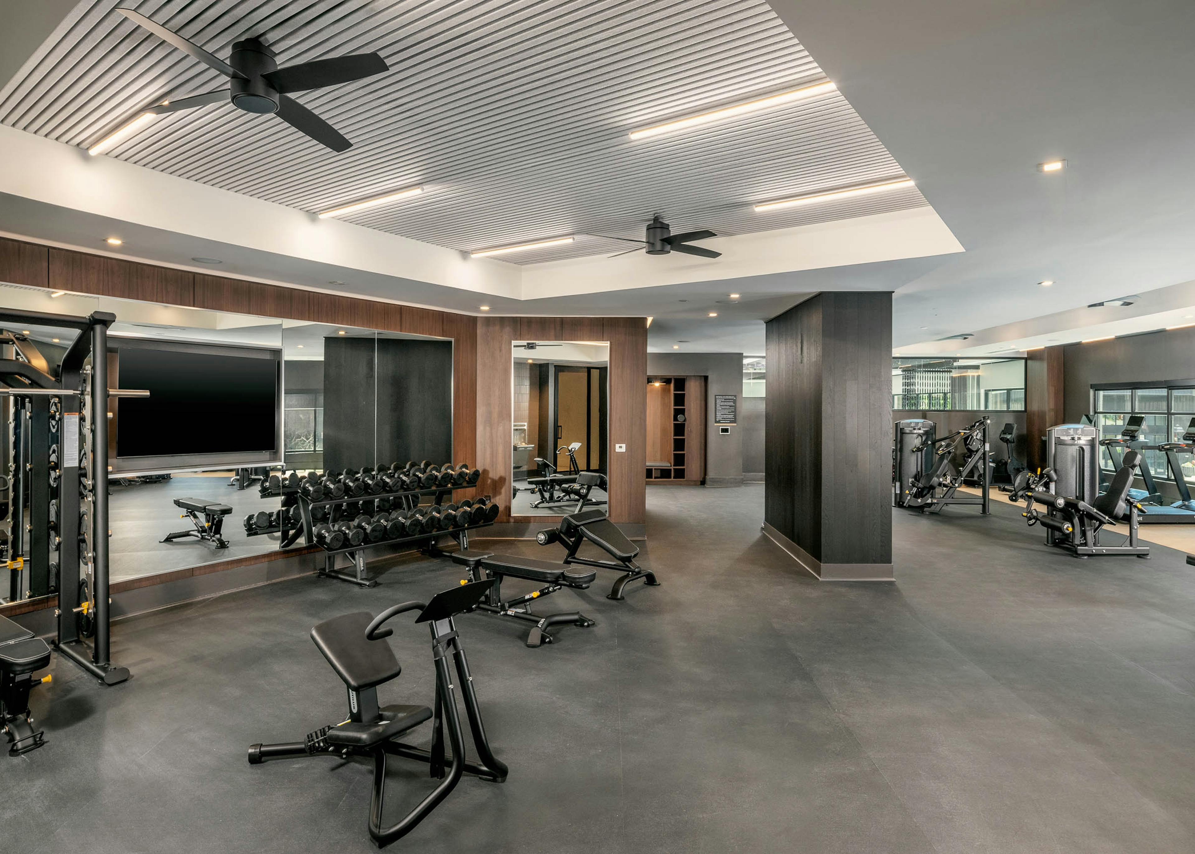 Spacious fitness center at AMLI Brookhaven apartments with a bench press and free weights and a full length mirror with ceiling fans
