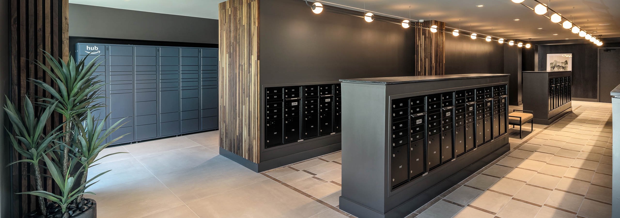 AMLI Brookhaven mailroom with tile flooring and track lighting and long rows of matte black mailboxes and Amazon hub lockers