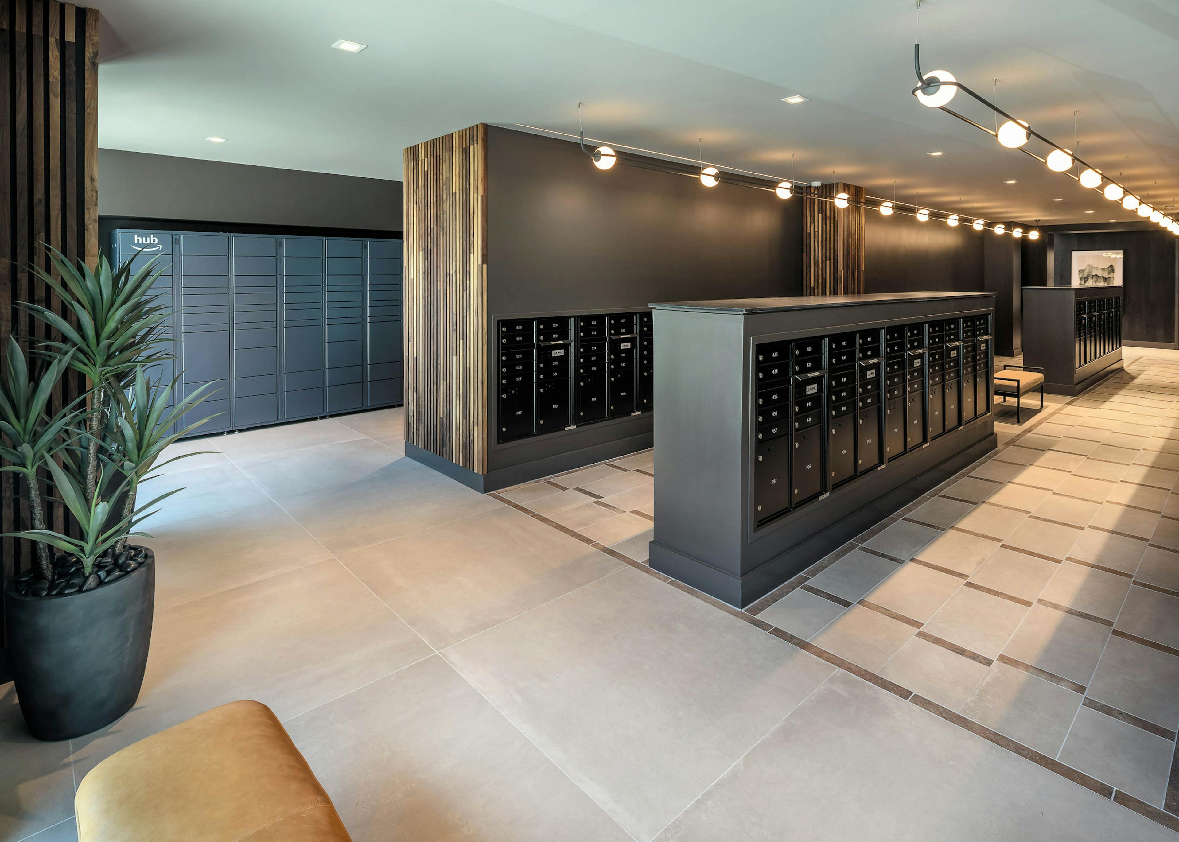 AMLI Brookhaven mailroom with tile flooring and track lighting and long rows of matte black mailboxes and Amazon hub lockers