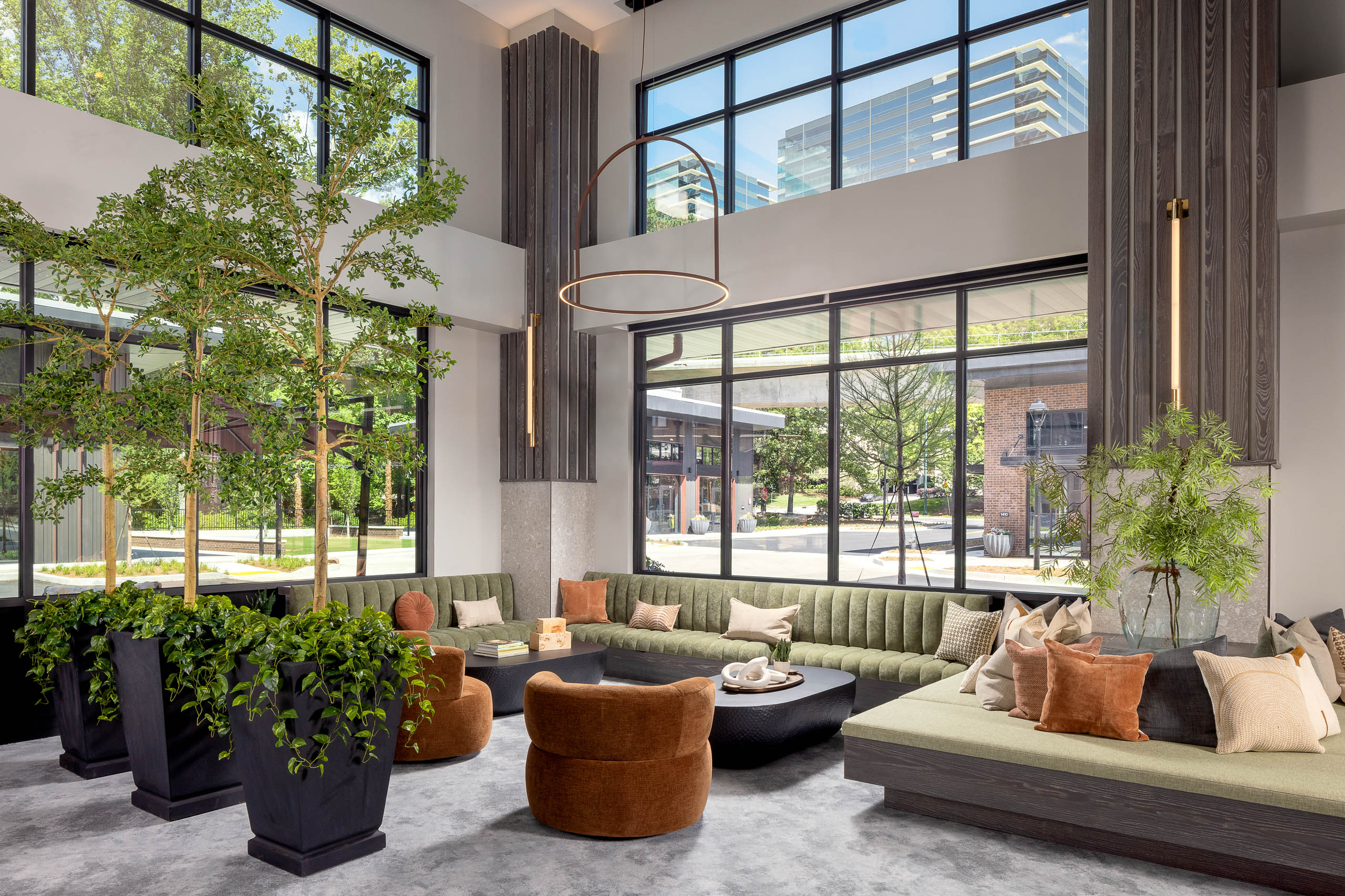 AMLI Brookhaven leasing office seating area with tall plants, green couches, tan chairs and a view to the street