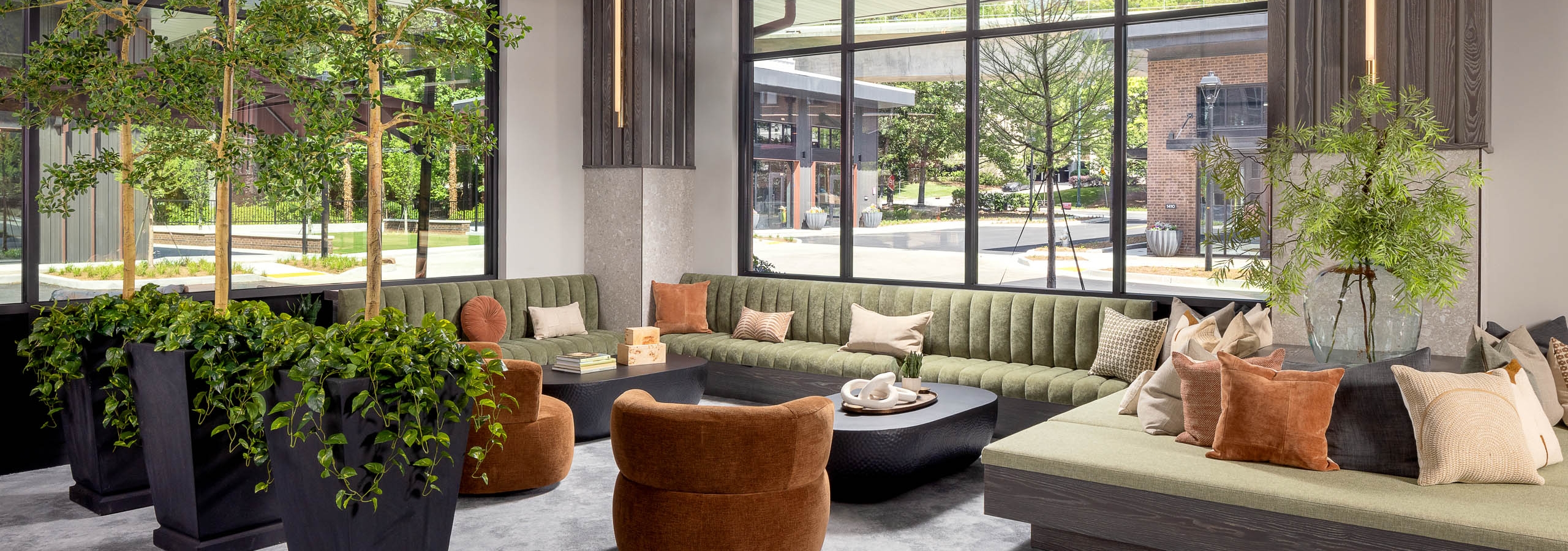 AMLI Brookhaven leasing office seating area with tall plants, green couches, tan chairs and a view to the street
