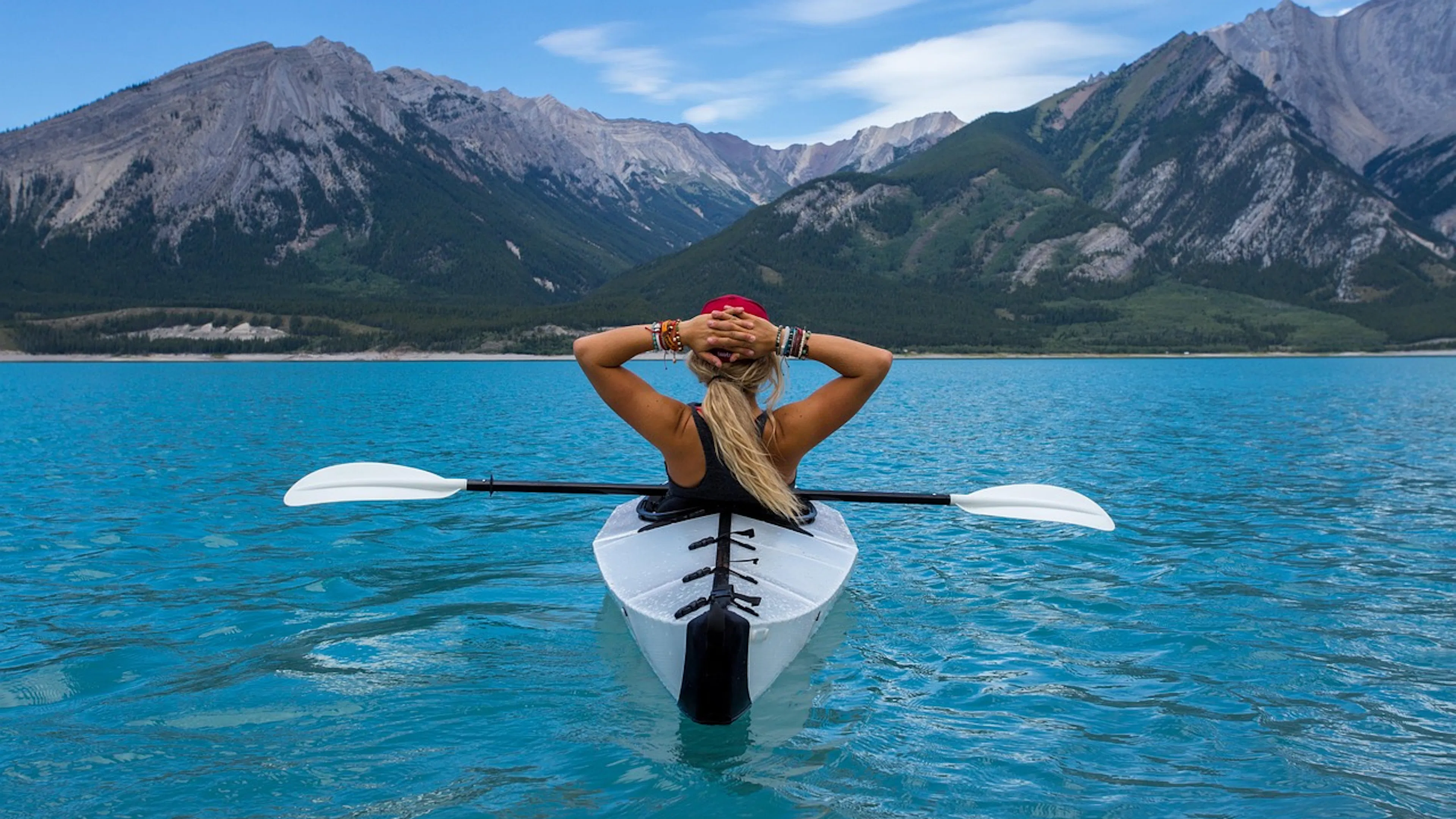 woman in white kayak on blue water in front of mountains