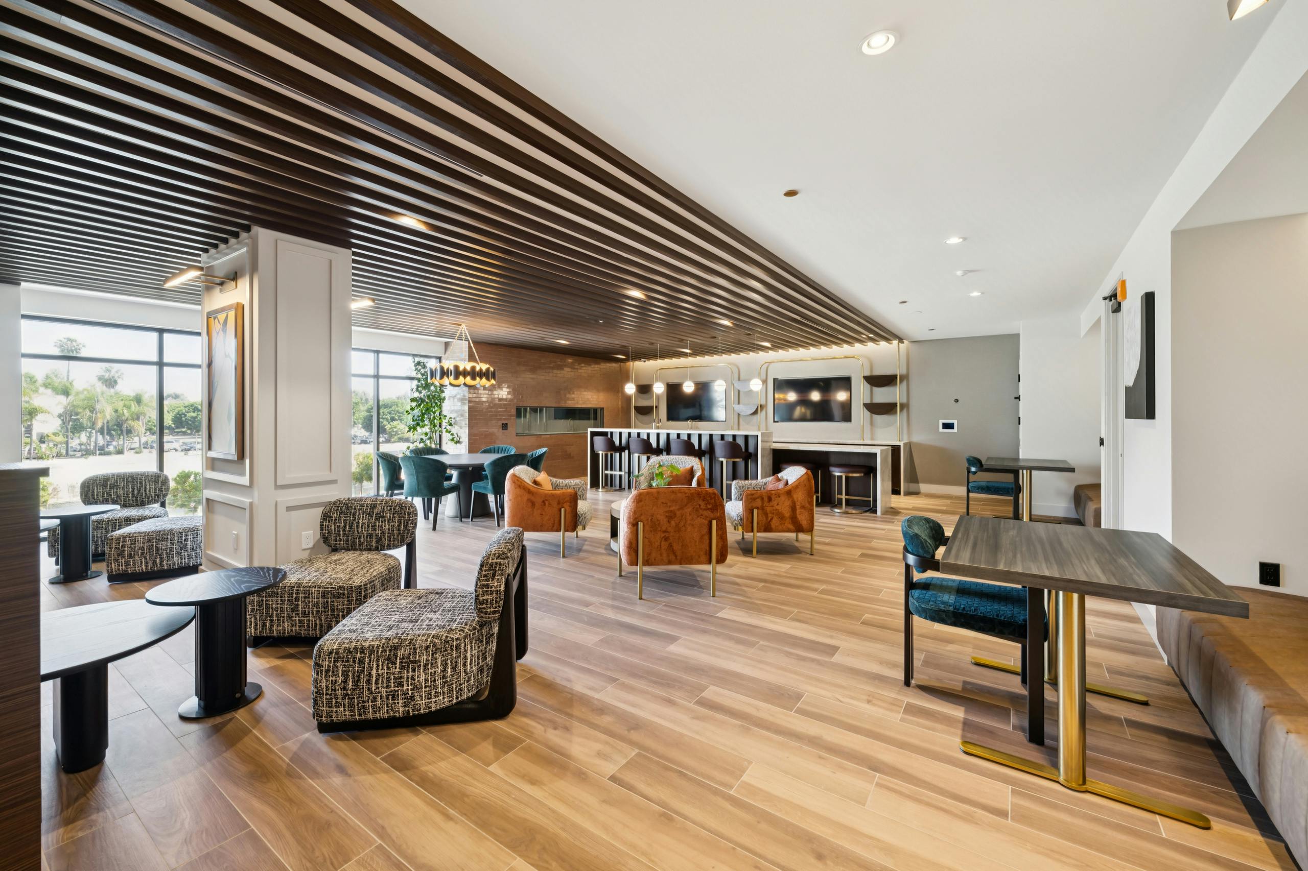 Lounge at AMLI Aero apartments with velvet seating, bar area, dining tables, wood plank floors, pendant lighting, and wall-mounted TV.