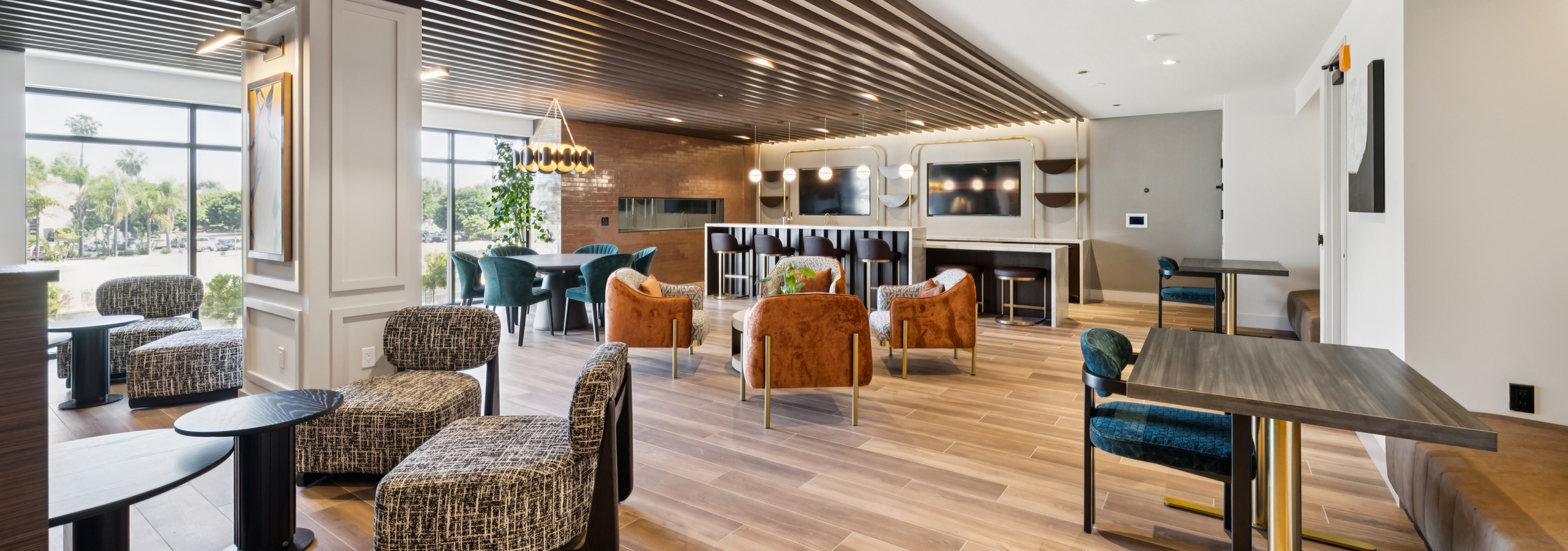 Lounge at AMLI Aero apartments with velvet seating, bar area, dining tables, wood plank floors, pendant lighting, and wall-mounted TV.