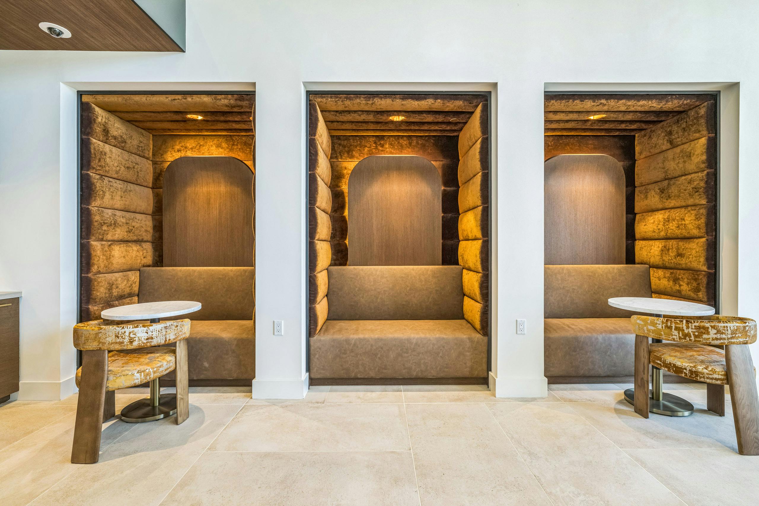Lounge pods at AMLI Aero apartments with gold velvet walls and booth seating, soft lighting, and round tables for private work.
