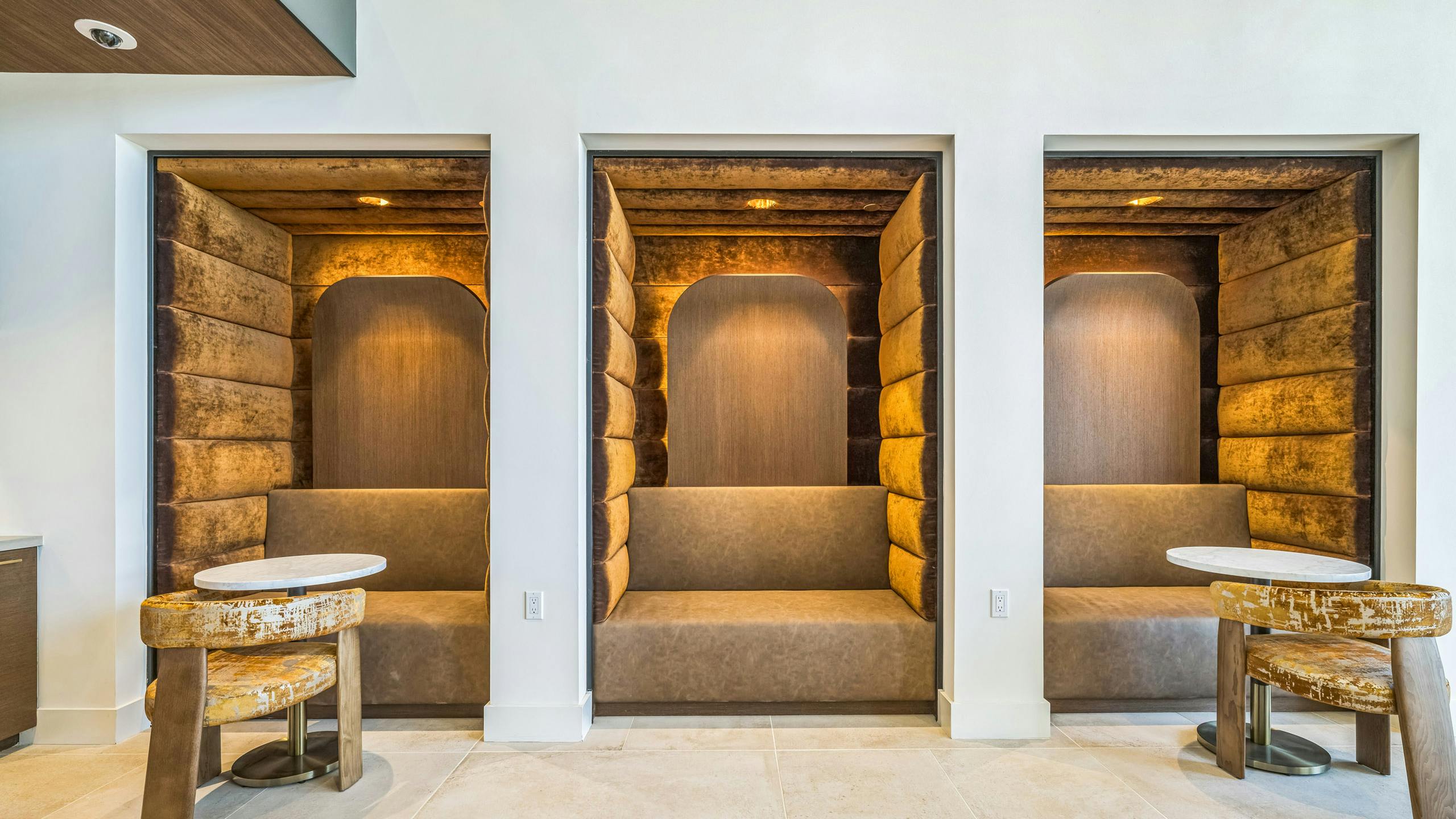 Lounge pods at AMLI Aero apartments with gold velvet walls and booth seating, soft lighting, and round tables for private work.