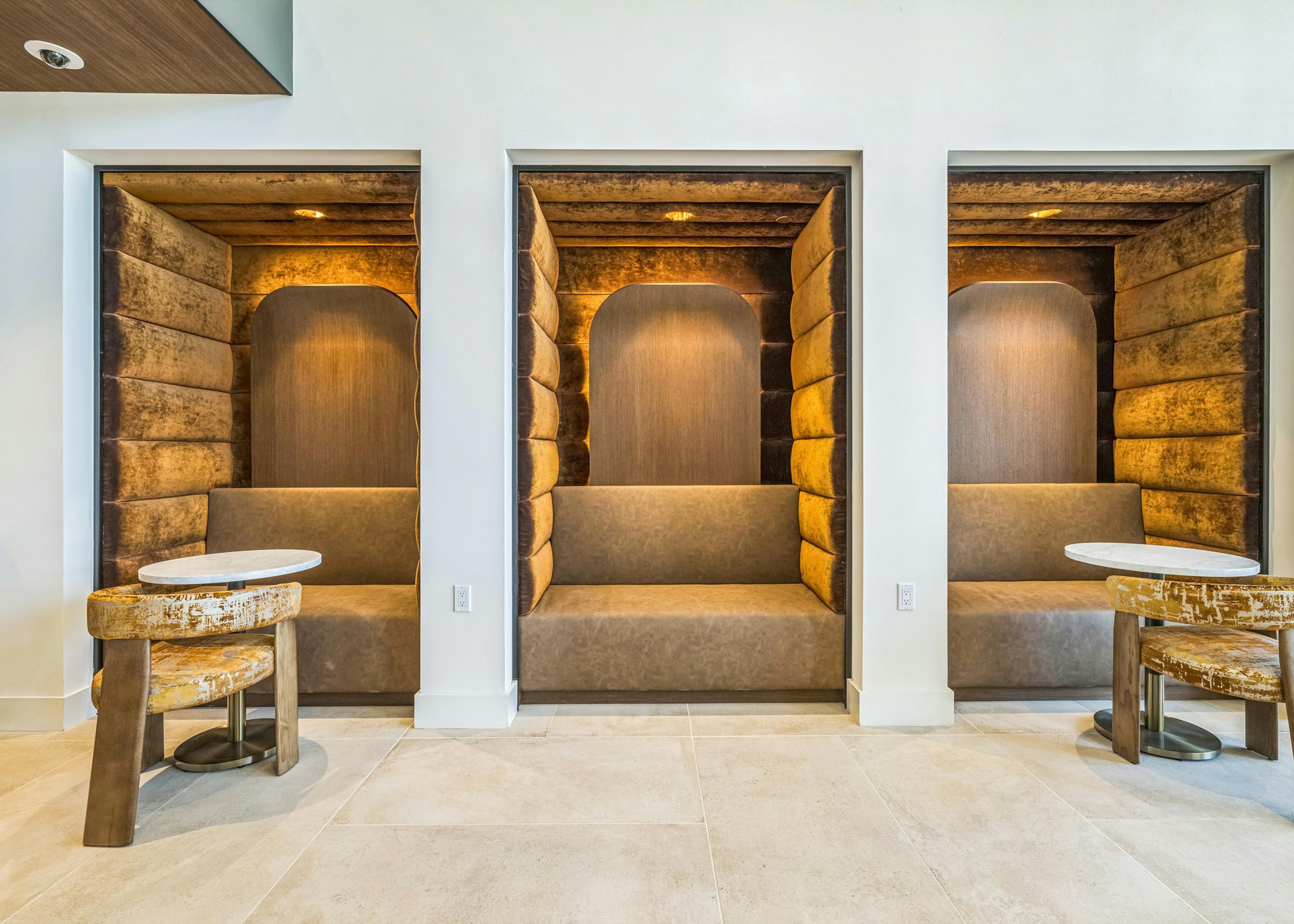 Lounge pods at AMLI Aero apartments with gold velvet walls and booth seating, soft lighting, and round tables for private work.