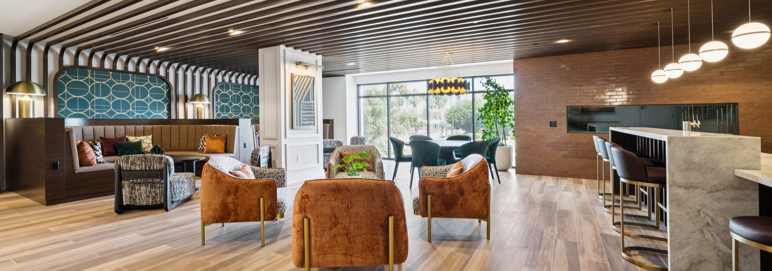 Open lounge at AMLI Aero apartments with rust colored chairs, booths, modern lighting, fireplace, and floor-to-ceiling windows.