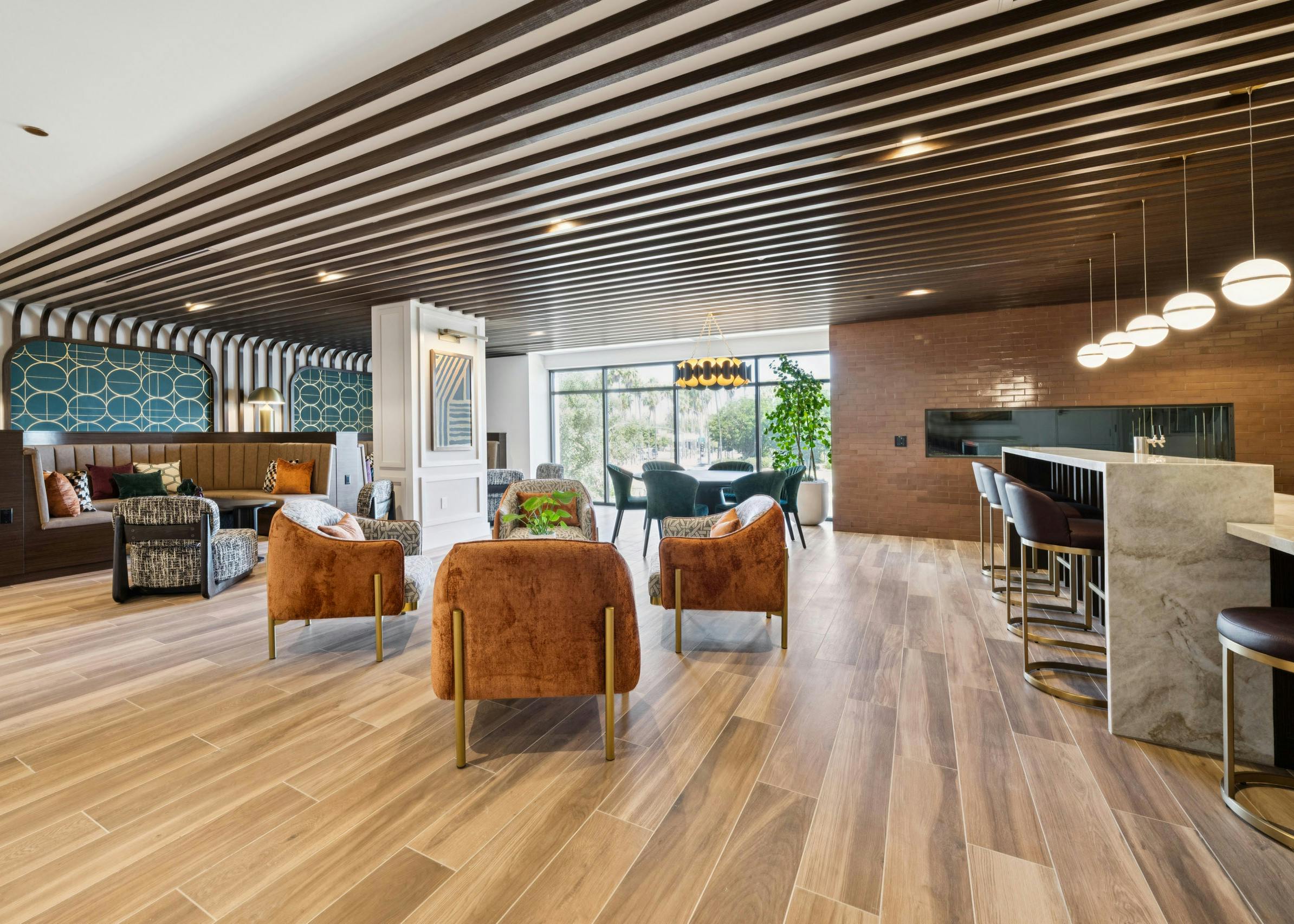 Open lounge at AMLI Aero apartments with rust colored chairs, booths, modern lighting, fireplace, and floor-to-ceiling windows.