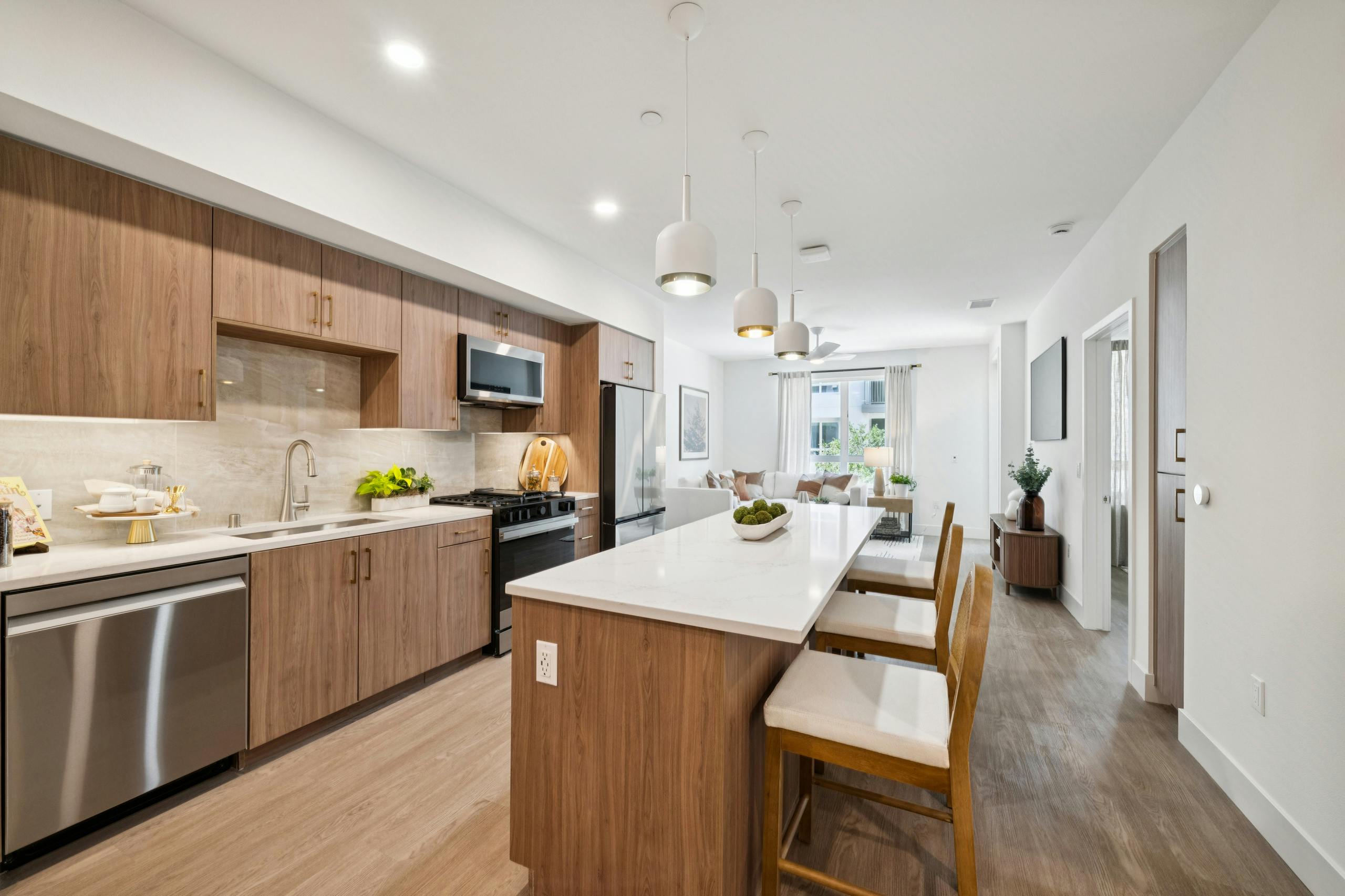 Large island kitchen at AMLI Aero with stainless steel appliances, wood cabinets, light quartz countertops and view to living room.