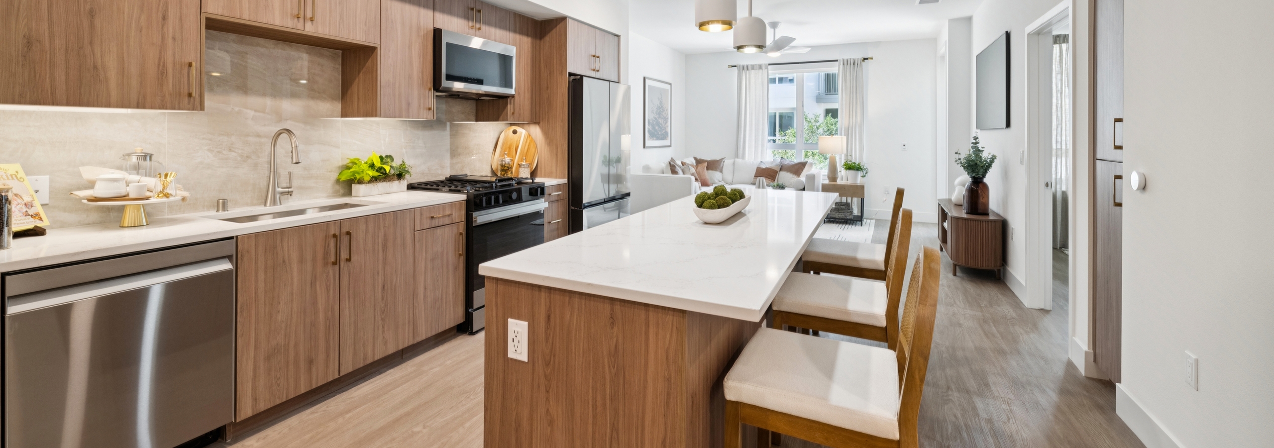 Large island kitchen at AMLI Aero  with stainless steel appliances, wood cabinets, light quartz  countertops and  view to living room.
