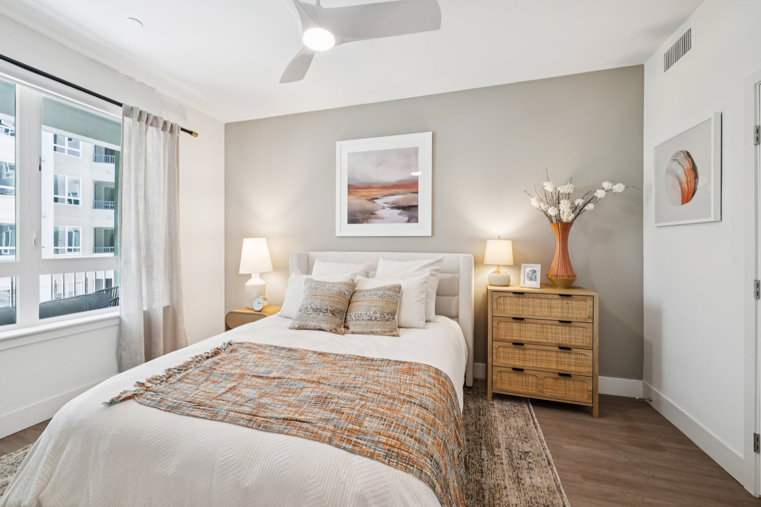 Interior view of AMLI Aero apartment bedroom with leather headboard, wooden nightstand and dresser, and large, curtained window