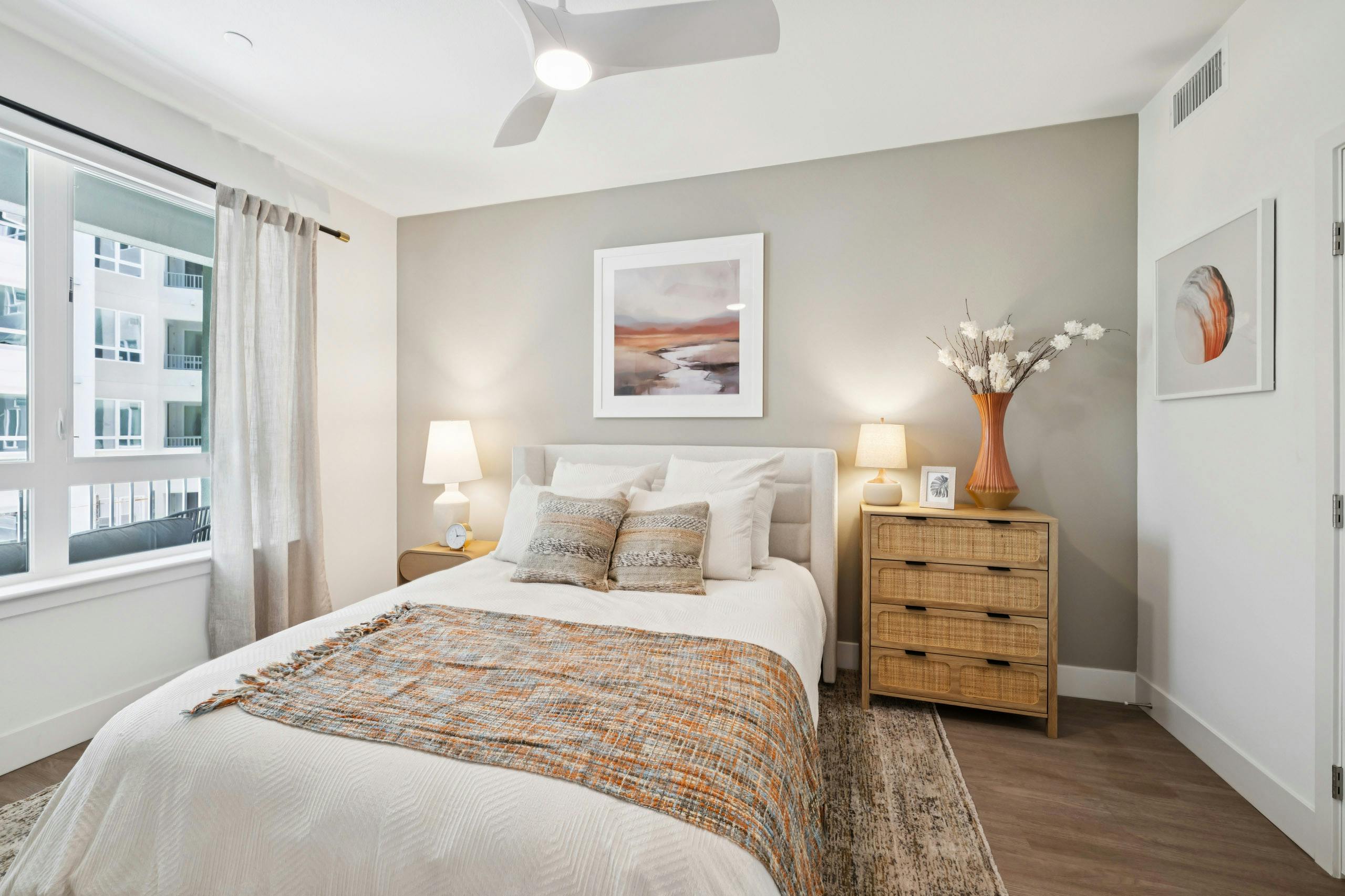 Interior view of AMLI Aero apartment bedroom with leather headboard, wooden nightstand and dresser, and large, curtained window