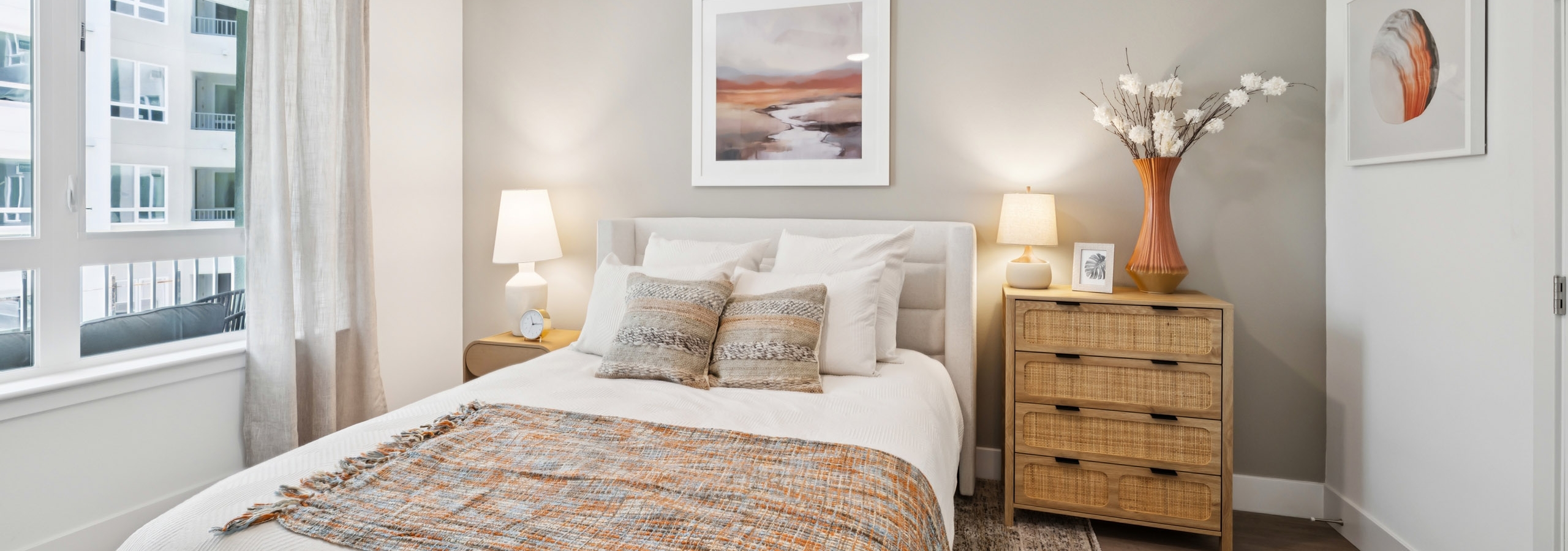 Interior view of AMLI Aero apartment bedroom with leather headboard, wooden nightstand and dresser, and large, curtained window