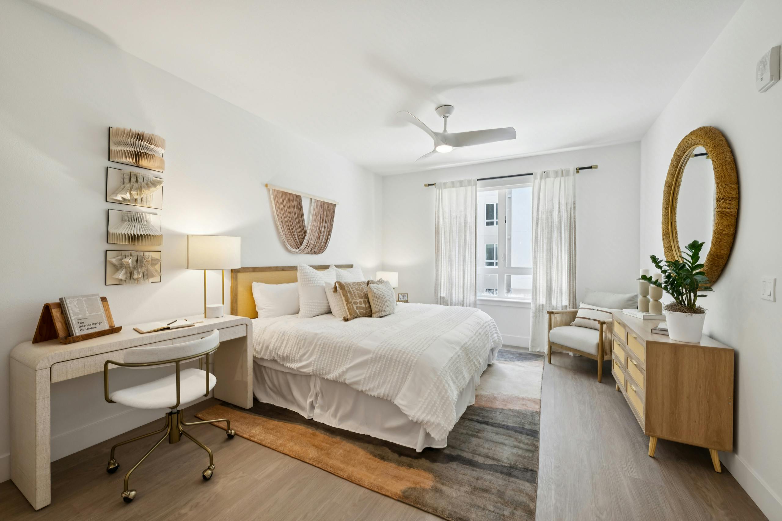 AMLI Aero apartment bedroom with king bed, layered pillows, writing desk with chair, ceiling fan, and large window with curtains.