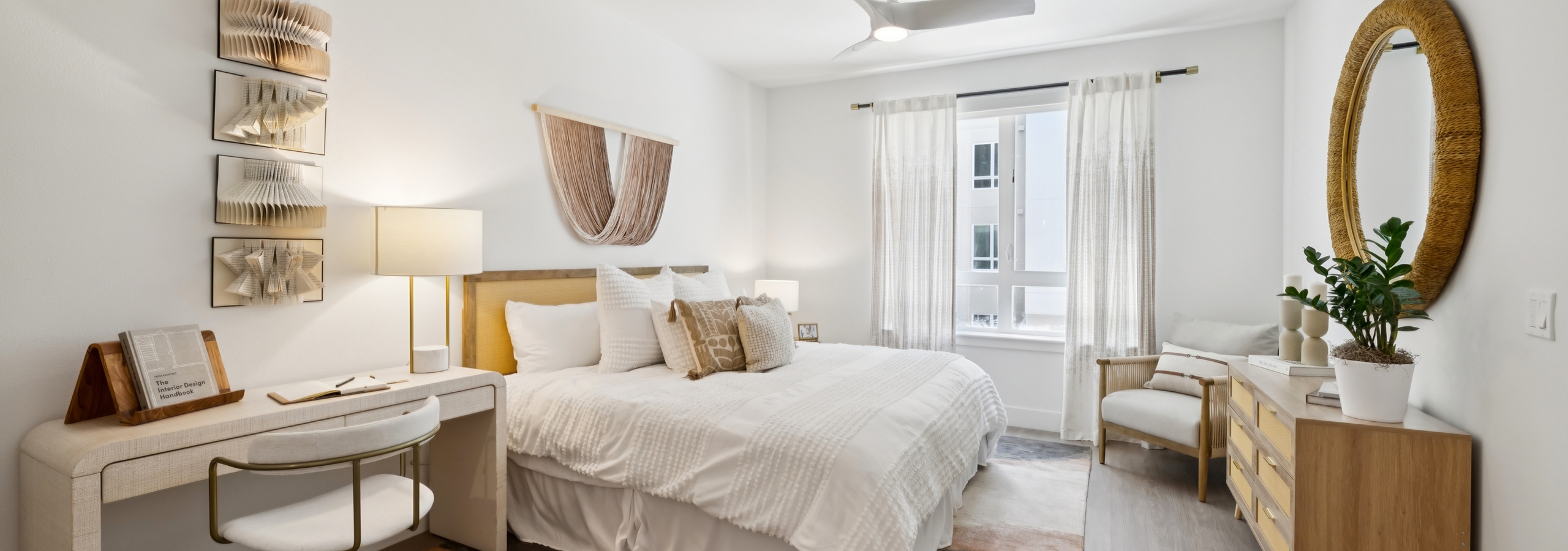 AMLI Aero apartment bedroom with king bed, layered pillows, writing desk with chair, ceiling fan, and large window with curtains.