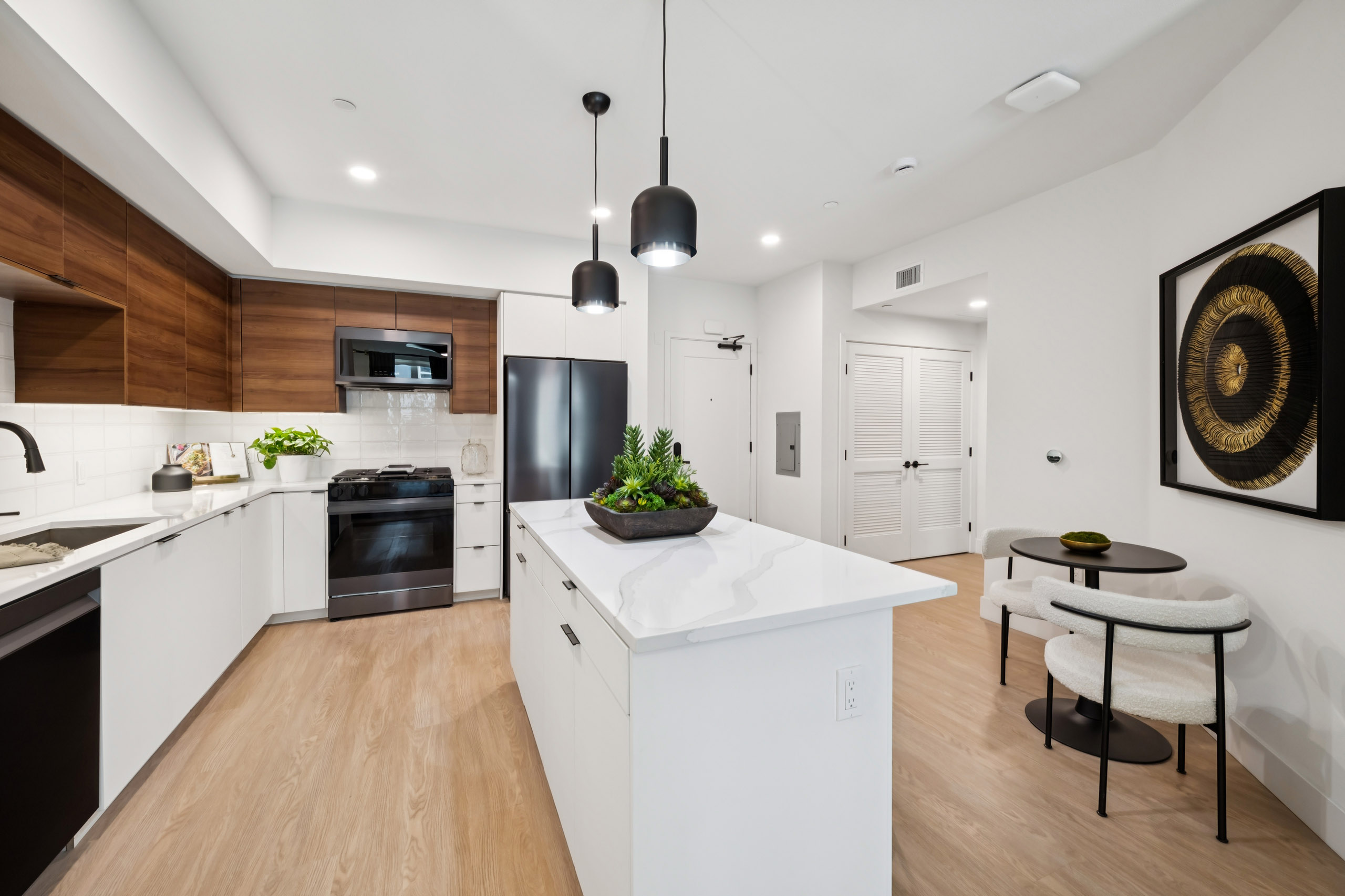 Kitchen at AMLI Aero with black appliances, white quartz island, black pendant lights, wood cabinets, and tile backsplash.