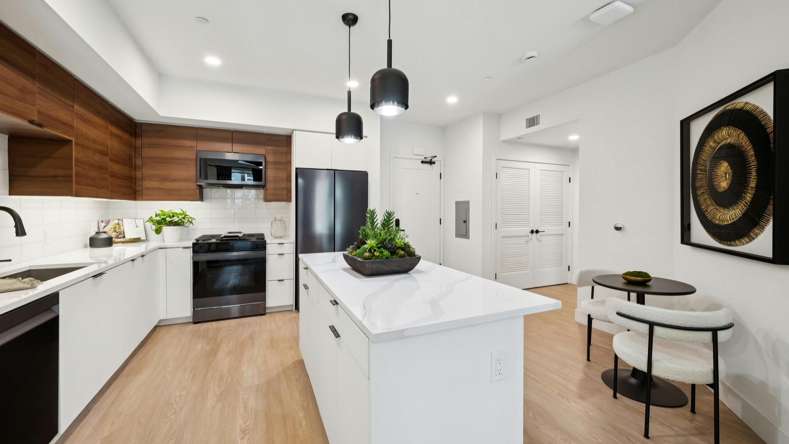 Kitchen at AMLI Aero with black appliances, white quartz island, black pendant lights, wood cabinets, and tile backsplash.