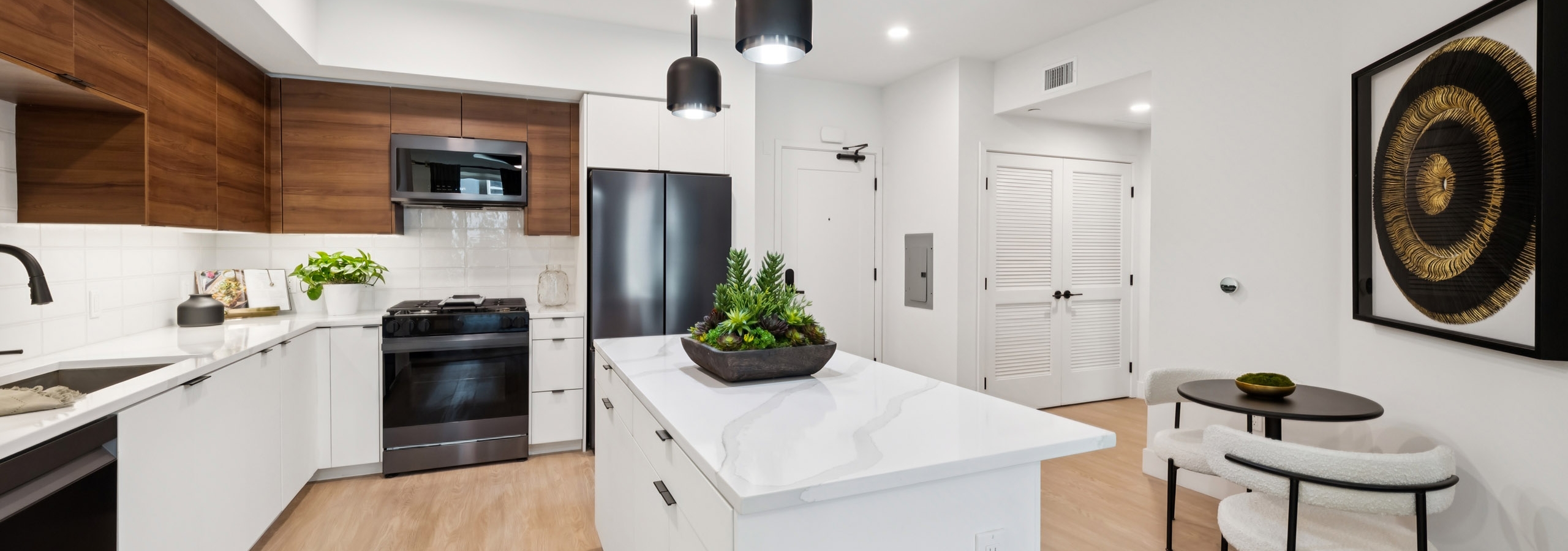 Kitchen at AMLI Aero with black appliances, white quartz island, black pendant lights, wood cabinets, and tile backsplash.