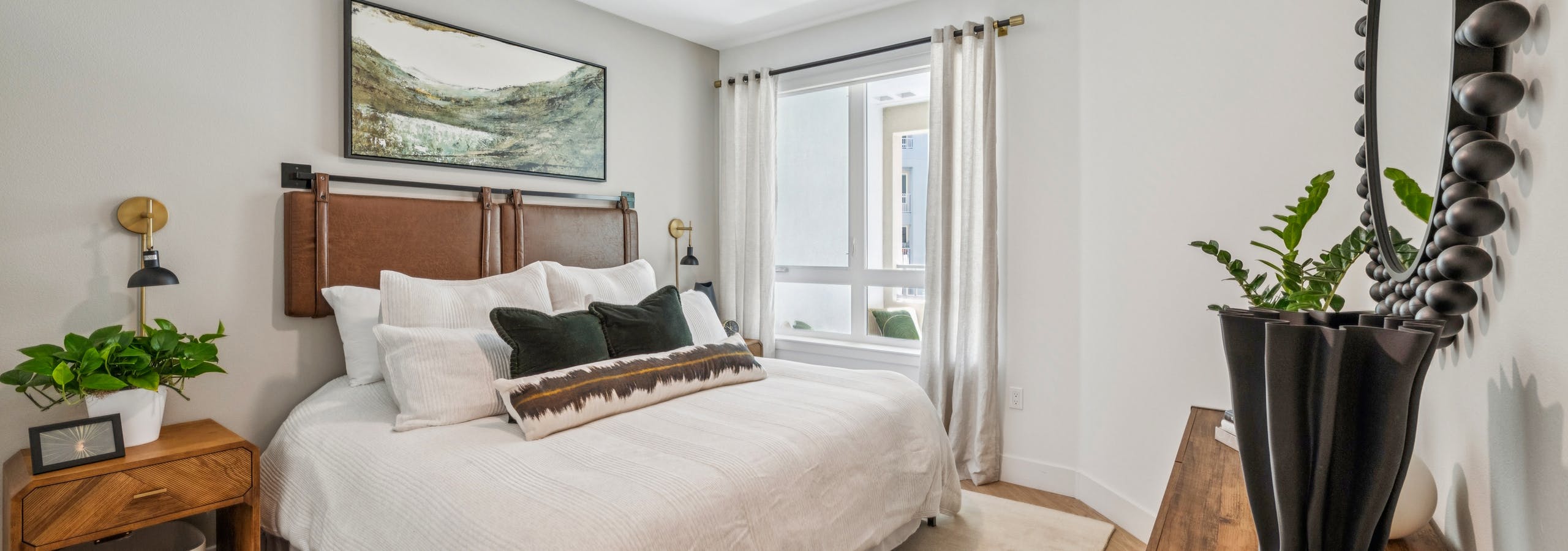 Stylish bedroom at AMLI Aero apartments with queen bed, textured throw blanket, wood nightstands, artwork, and large sunny window.