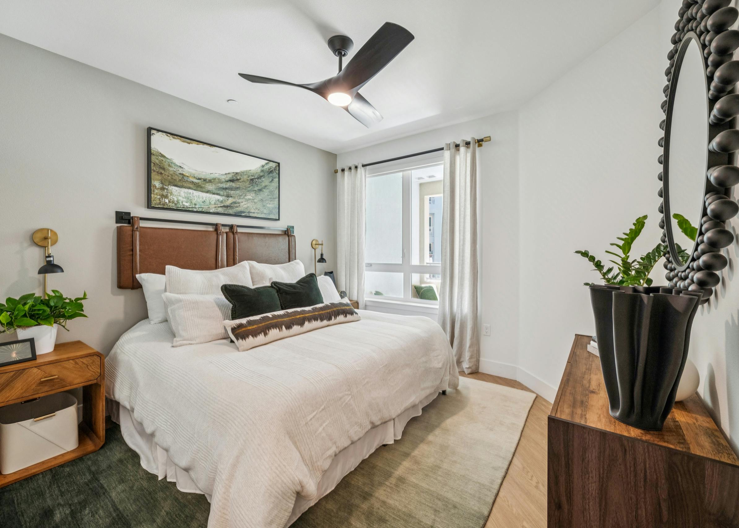 Stylish bedroom at AMLI Aero apartments with queen bed, textured throw blanket, wood nightstands, artwork, and large sunny window.