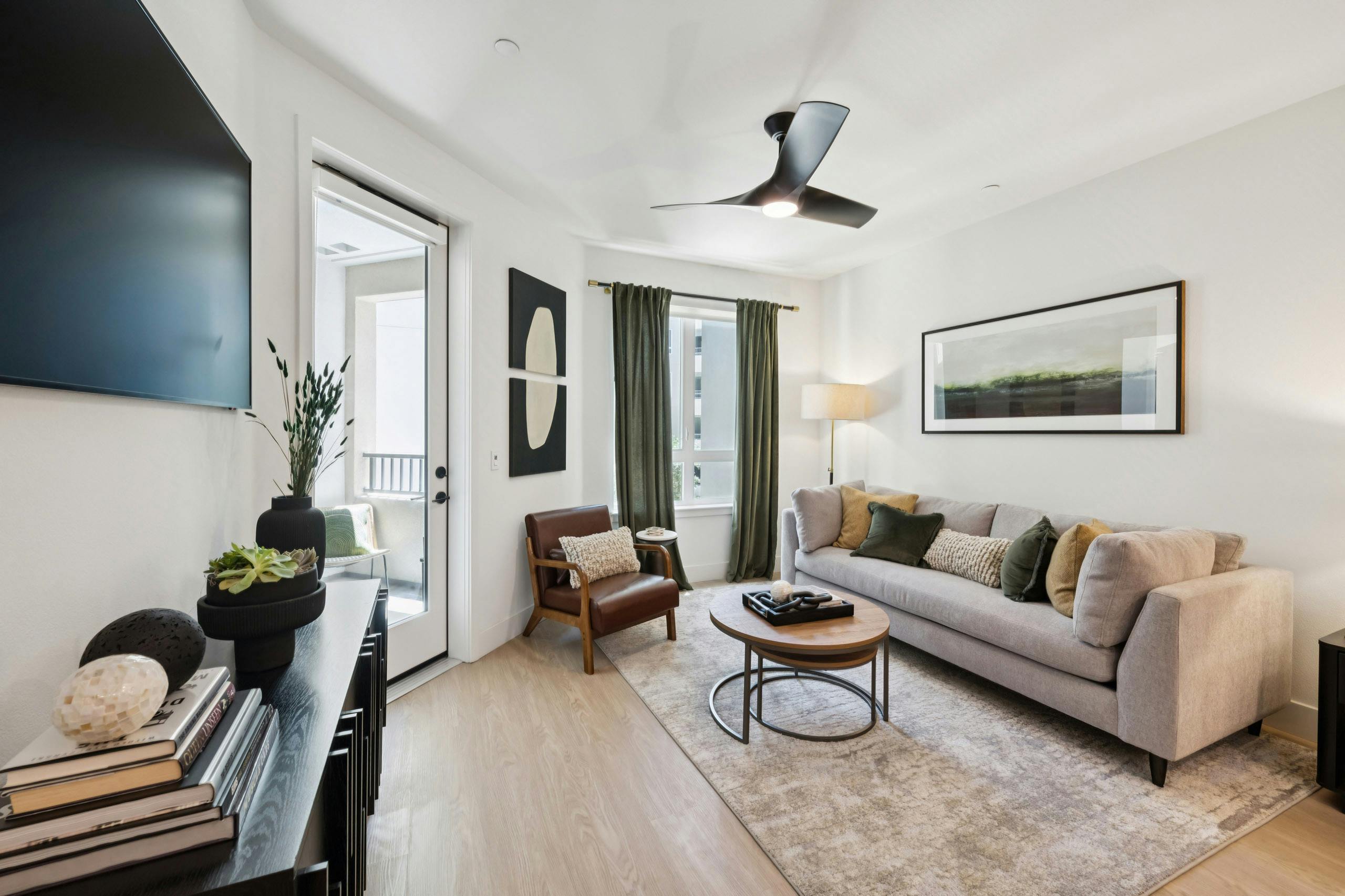 AMLI Aero apartment living room with taupe sofa on area rug, green accent pillows and curtains to match, coffee table, and wall-mounted TV.
