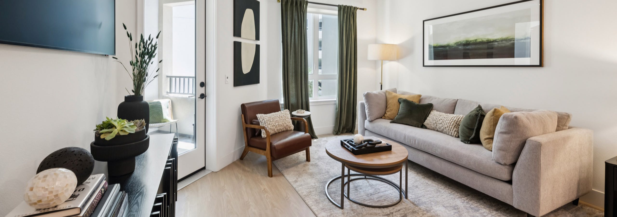 AMLI Aero apartment living room with taupe sofa on area rug, green accent pillows and curtains to match, coffee table, and wall-mounted TV.