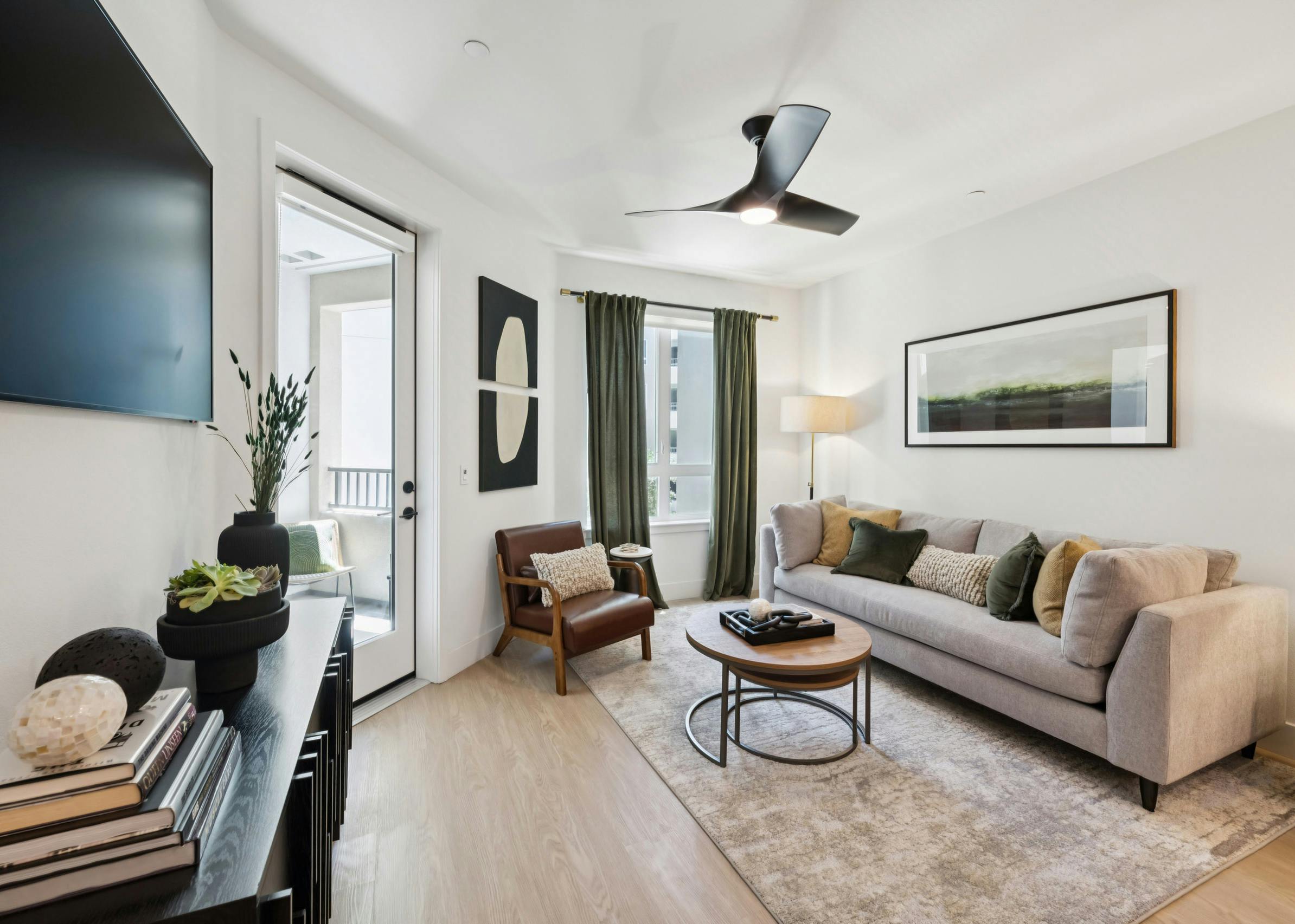 AMLI Aero apartment living room with taupe sofa on area rug, green accent pillows and curtains to match, coffee table, and wall-mounted TV.