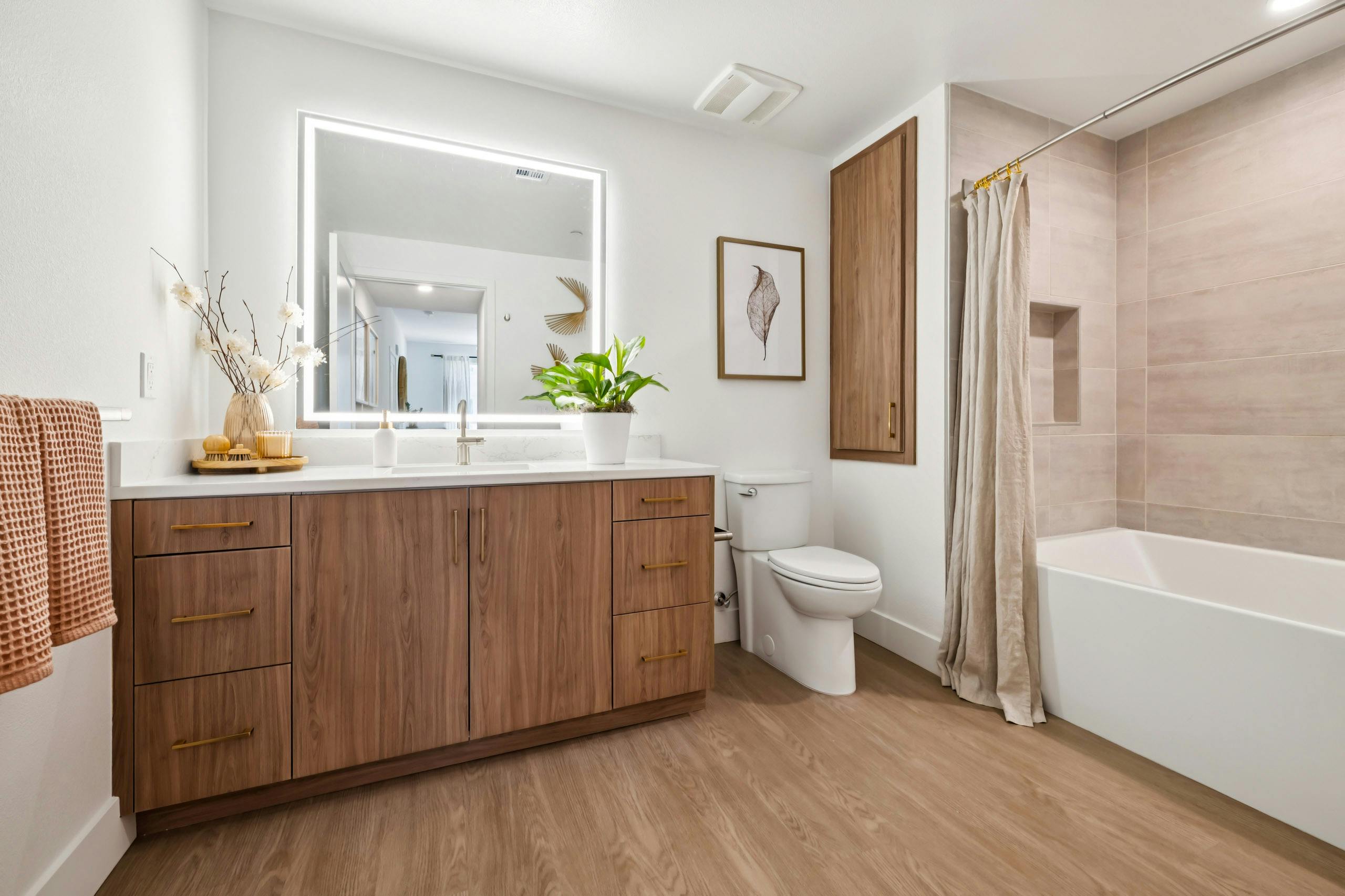 Sleek bathroom at AMLI Aero apartments with wide wood vanity, LED mirror, modern faucet, light tile shower, and brass drawer handles.