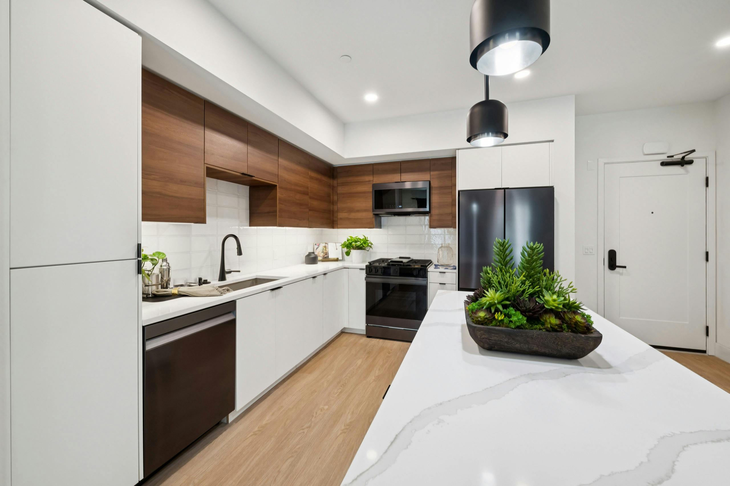 AMLI Aero kitchen with black appliances, white quartz island, black pendant lights, and tile backsplash.