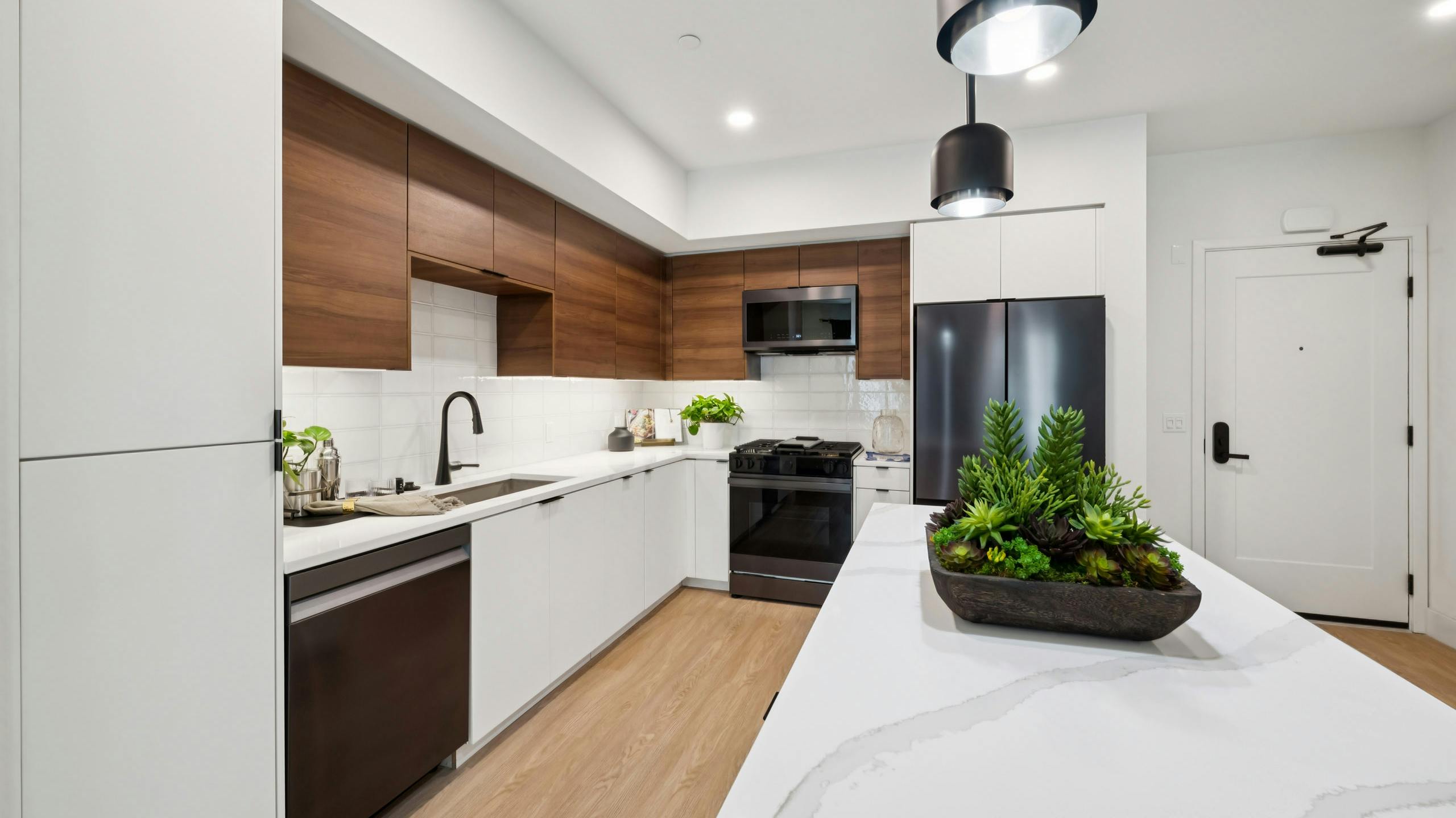 AMLI Aero kitchen with black appliances, white quartz island, black pendant lights, and tile backsplash.