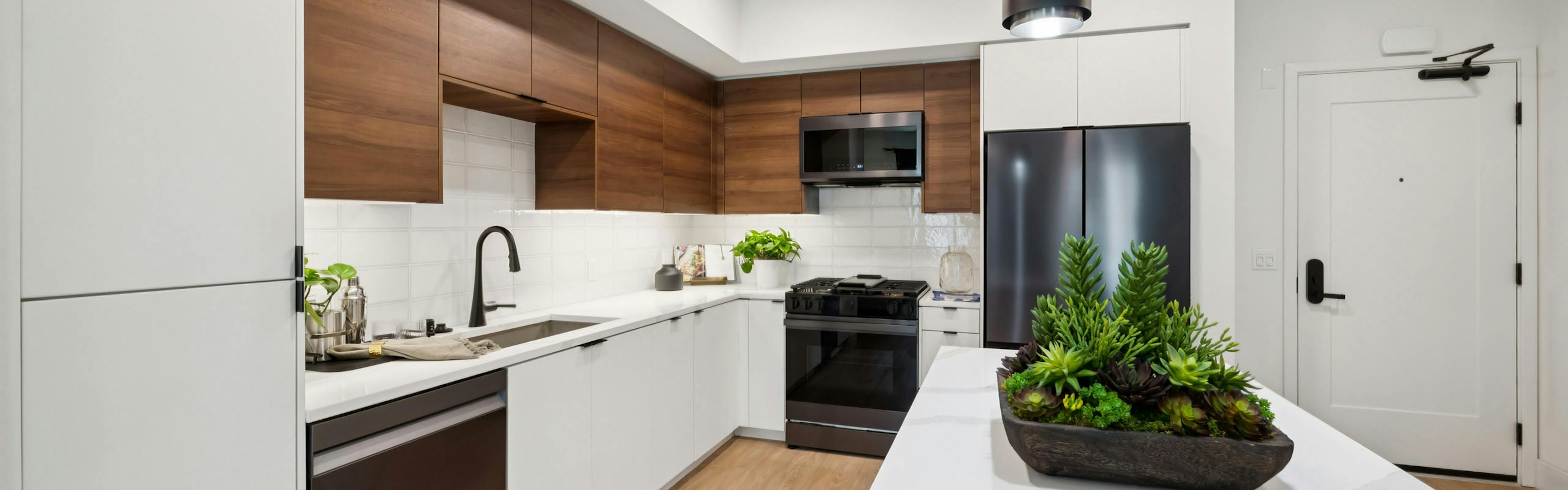 AMLI Aero kitchen with black appliances, white quartz island, black pendant lights, and tile backsplash.