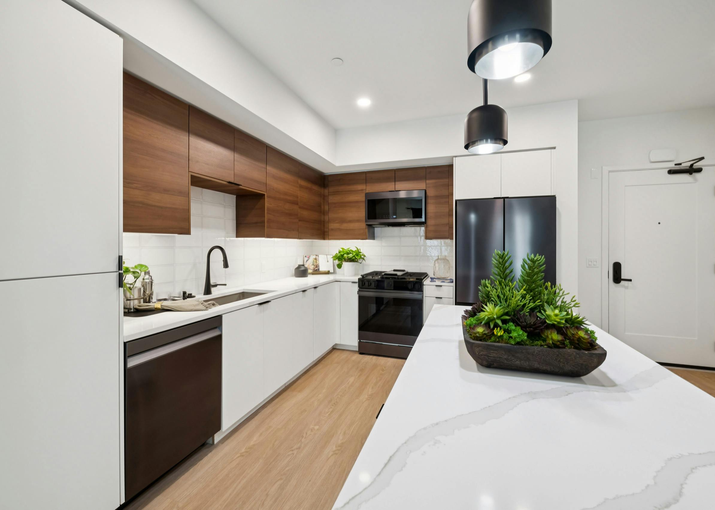 AMLI Aero kitchen with black appliances, white quartz island, black pendant lights, and tile backsplash.