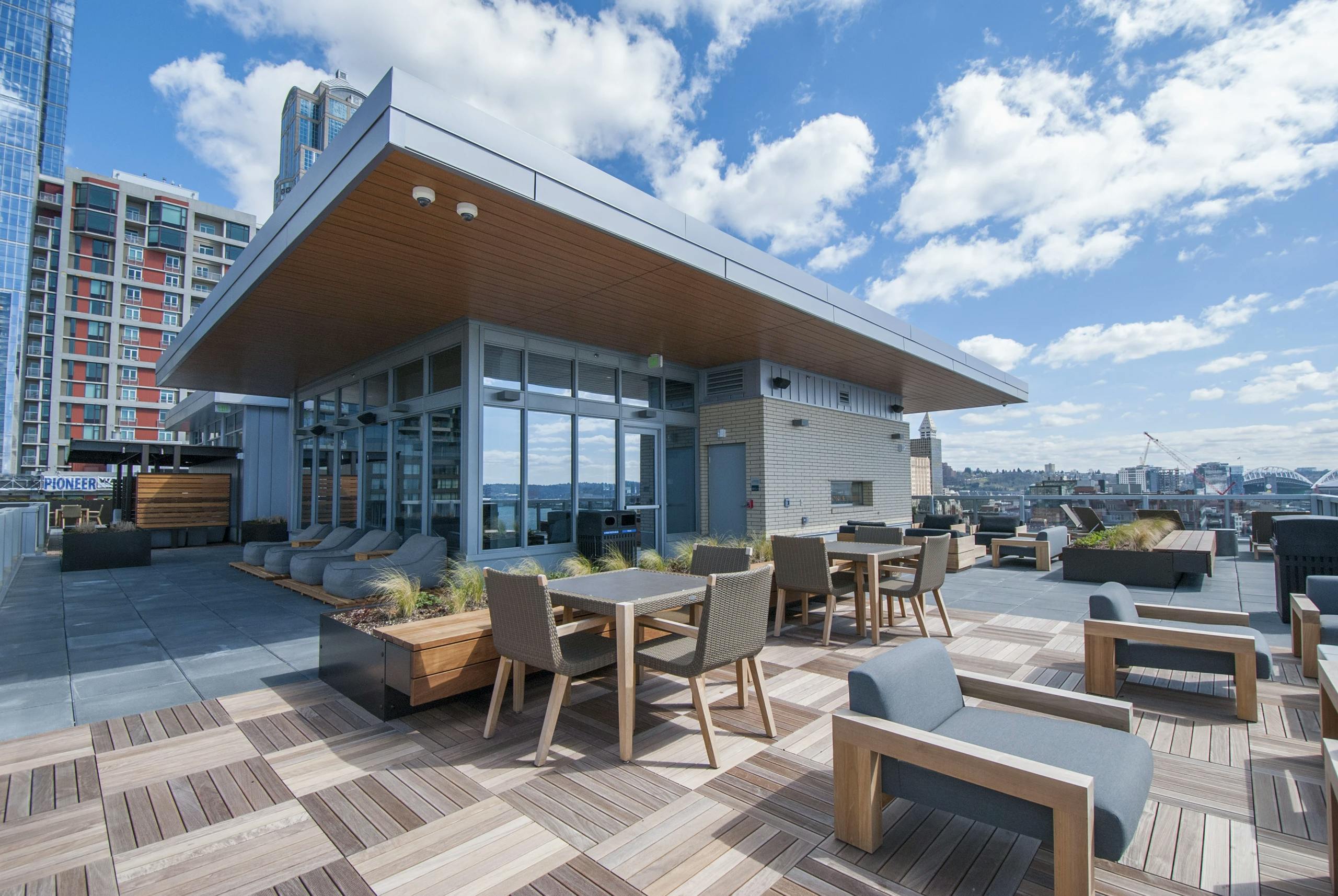 Rooftop terrace at AMLI Waterfront apartments with patio tables, planters, skyline backdrop, and entertainment room.