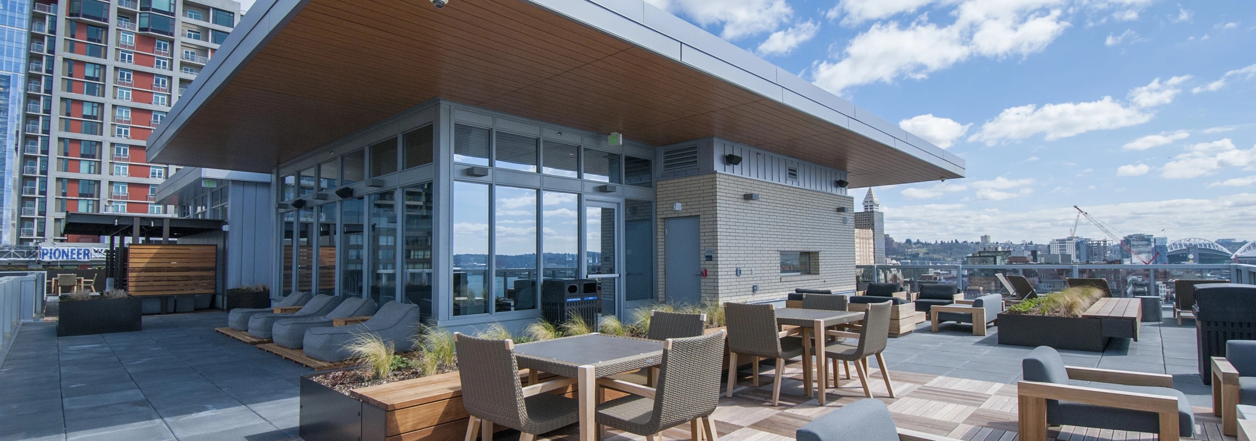Rooftop terrace at AMLI Waterfront apartments with patio tables, planters, skyline backdrop, and entertainment room.