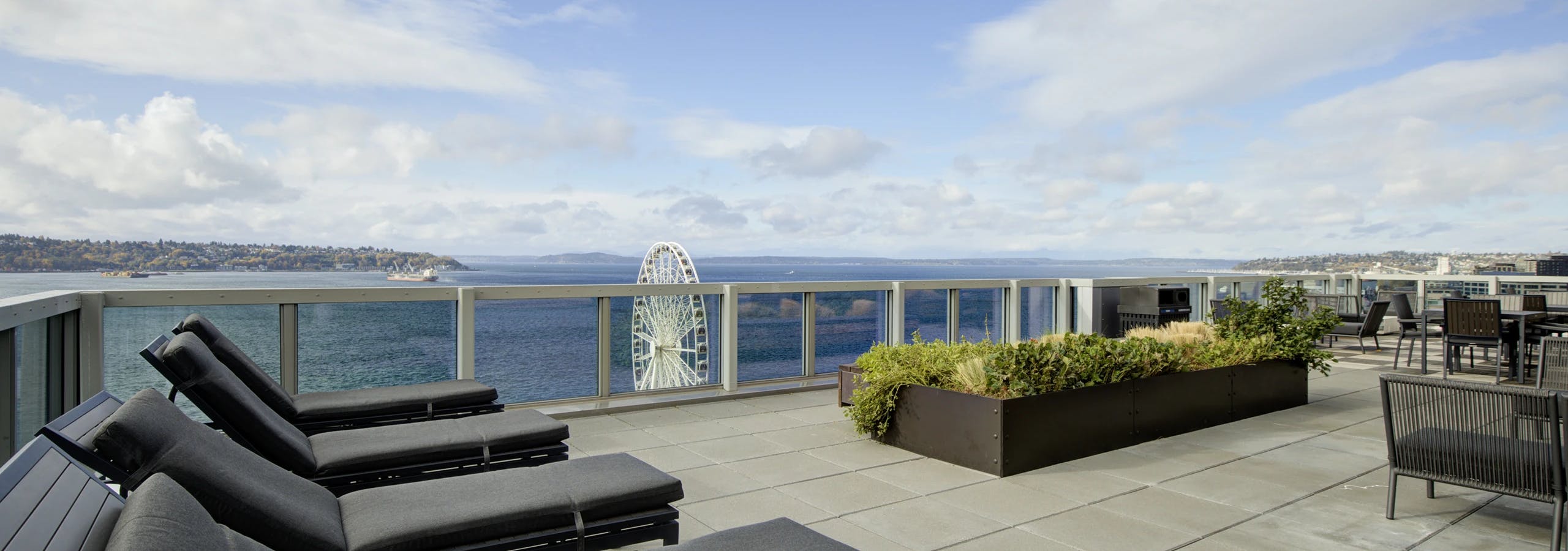 Rooftop deck with gray loungers, planter beds, and Puget Sound views on a sunny day at AMLI Waterfront apartments