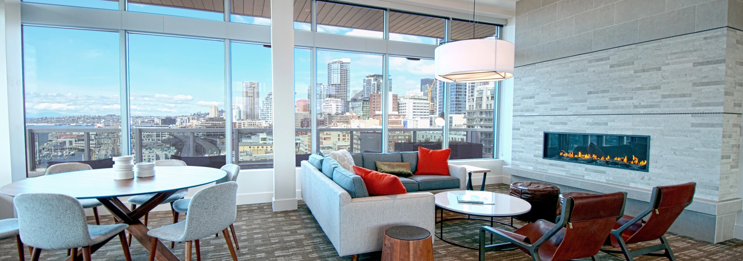 Rooftop clubroom at AMLI Waterfront apartments with sectional sofa, fireplace, leather chairs, and skyline views through tall windows.