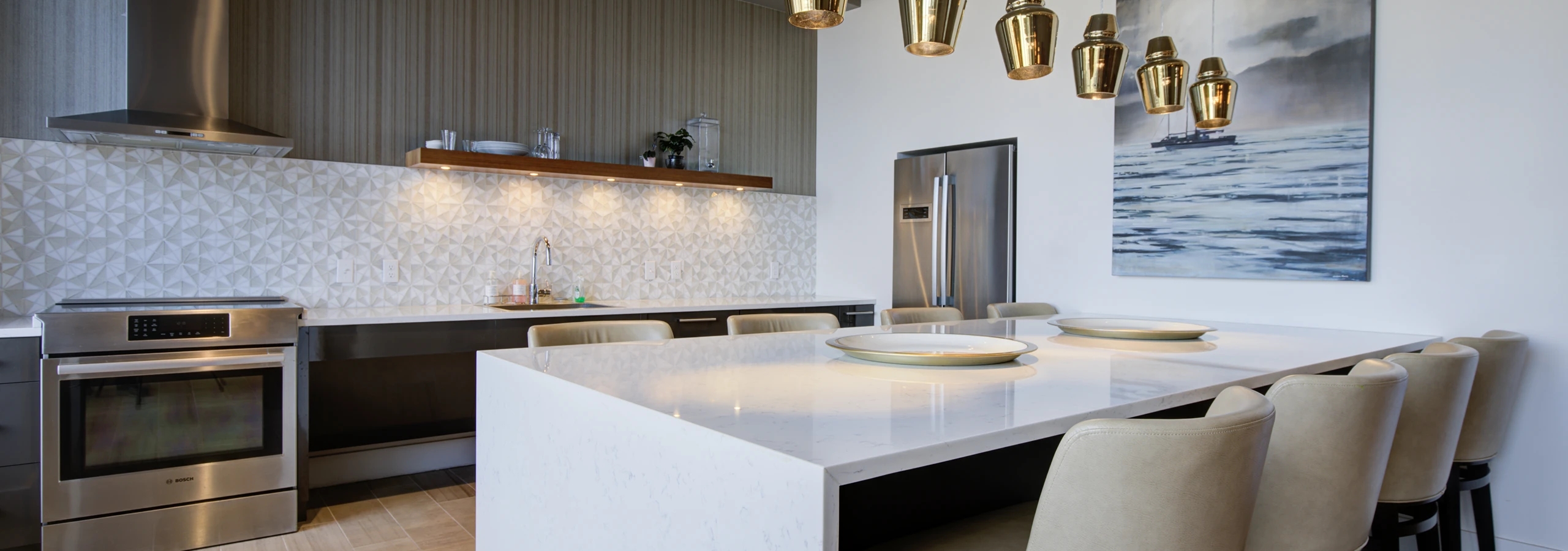 AMLI Waterfront clubroom kitchen at AMLI with quartz island, bar stools, gold pendant lighting, and full backsplash.