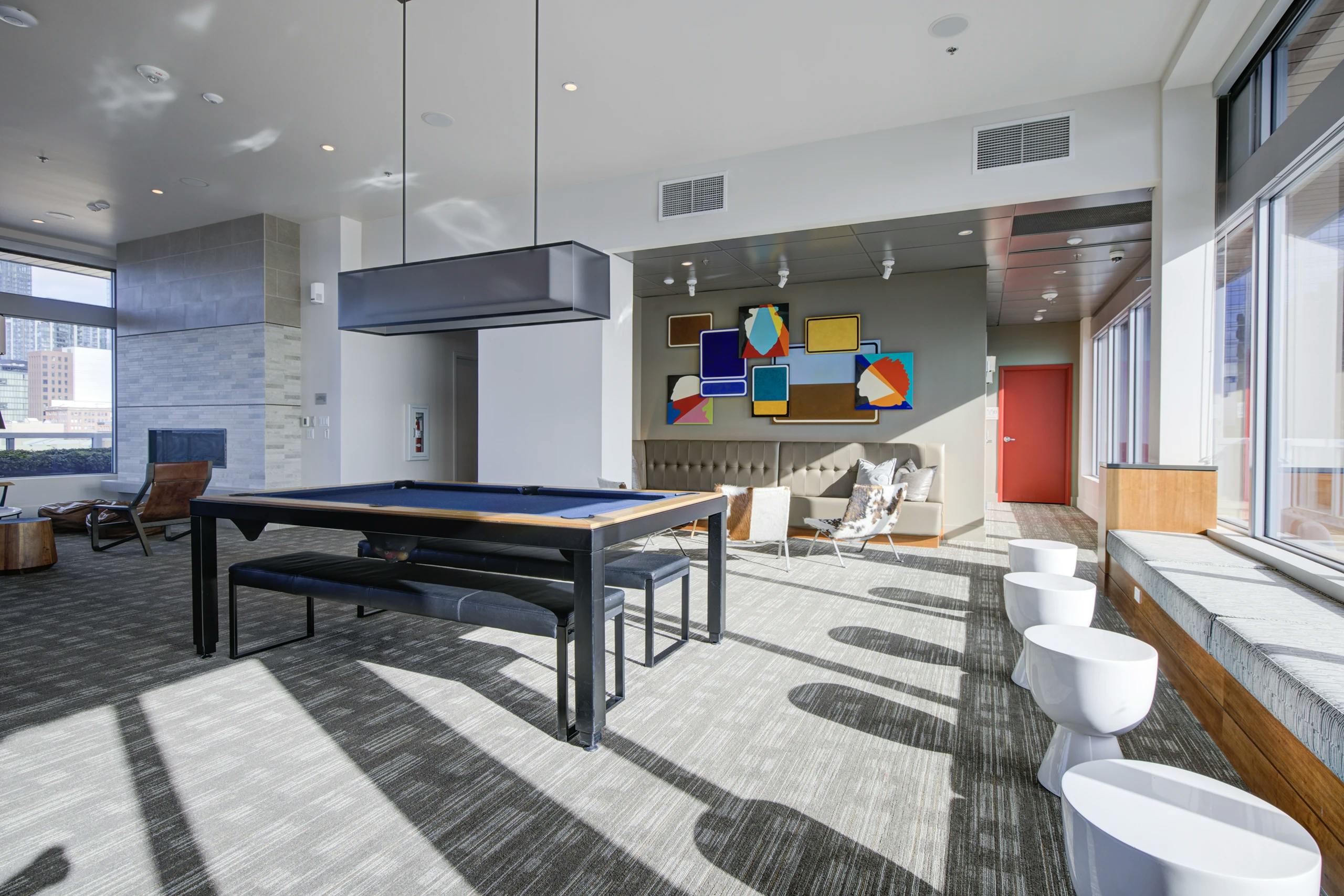 Clubroom at AMLI Waterfront apartments with pool table, colorful abstract art, bench seating, and natural light from tall windows.