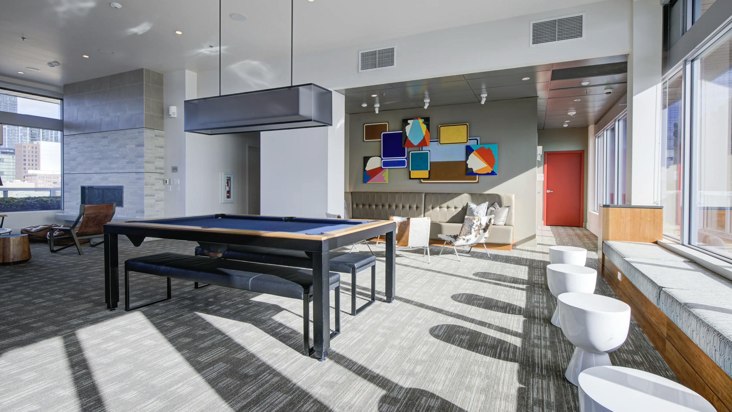Clubroom at AMLI Waterfront apartments with pool table, colorful abstract art, bench seating, and natural light from tall windows.