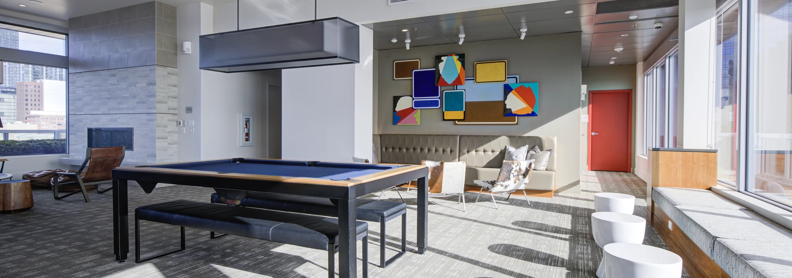 Clubroom at AMLI Waterfront apartments with pool table, colorful abstract art, bench seating, and natural light from tall windows.