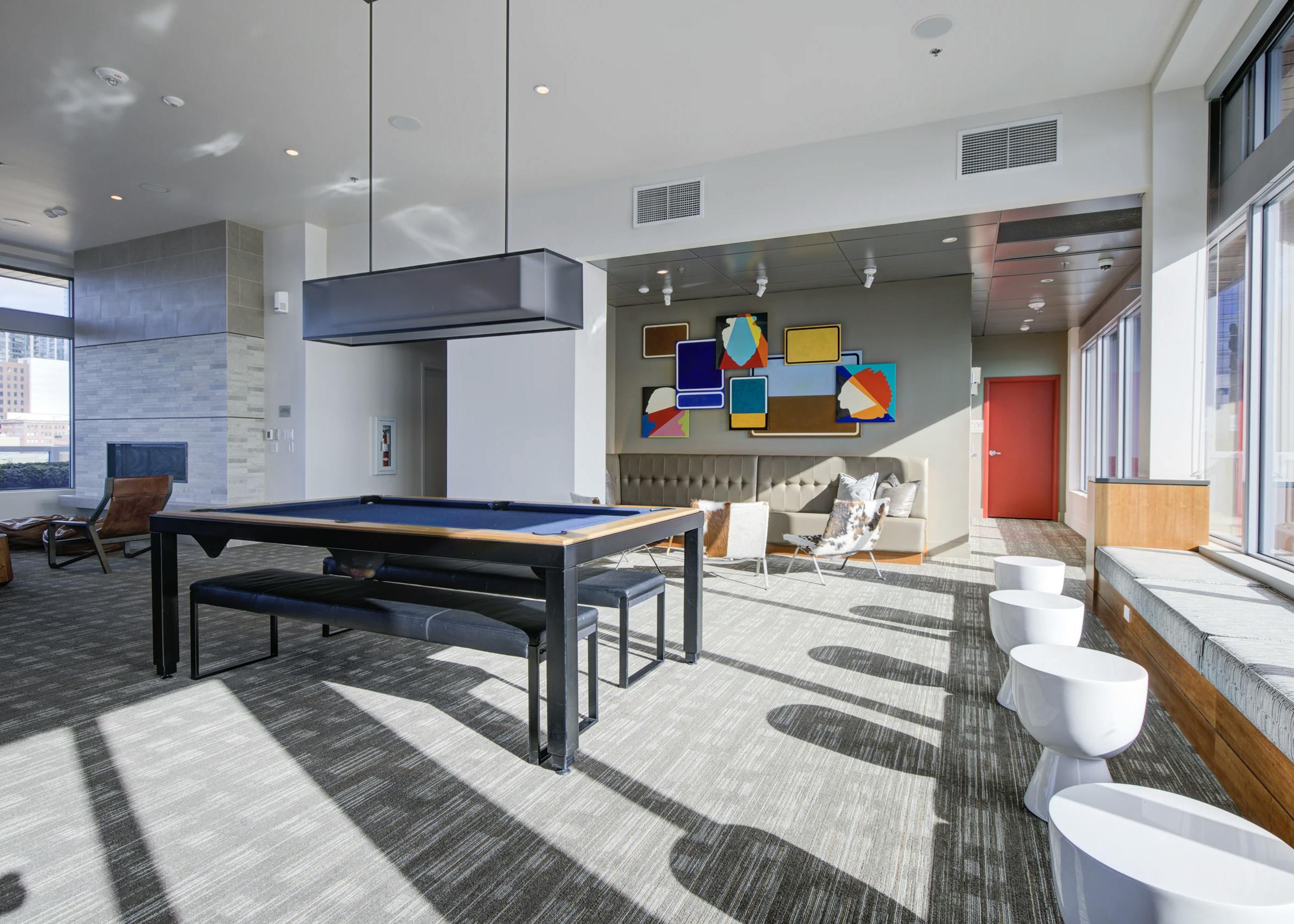 Clubroom at AMLI Waterfront apartments with pool table, colorful abstract art, bench seating, and natural light from tall windows.