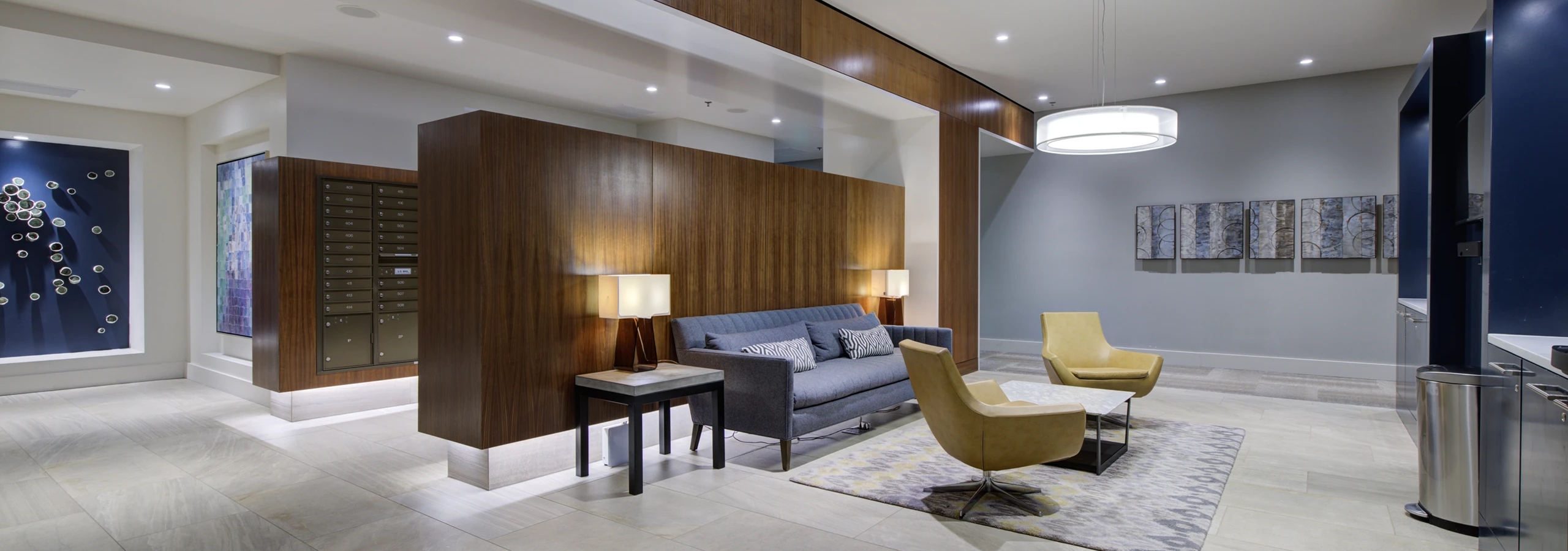 Lobby lounge at AMLI Waterfront apartments with gray sofa, yellow chairs, mail center, and wood-paneled accents.