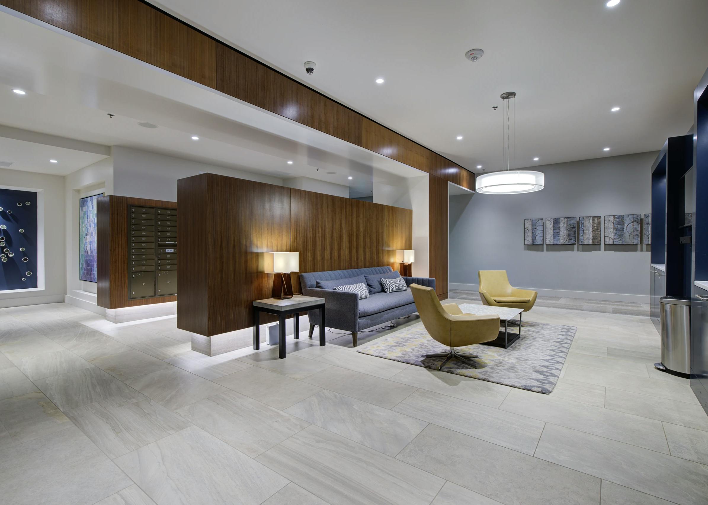 Lobby lounge at AMLI Waterfront apartments with gray sofa, yellow chairs, mail center, and wood-paneled accents.
