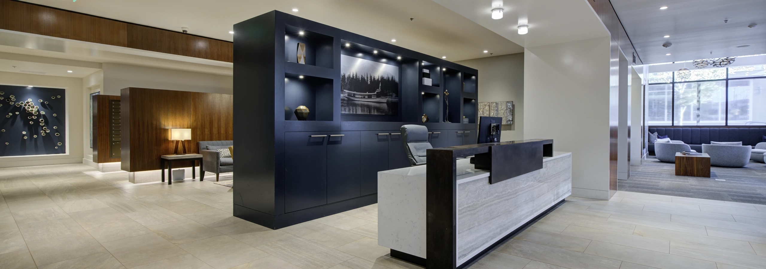 Open reception area at AMLI Waterfront apartments with navy shelving, wood and marble desk, and lounge seating in the background.