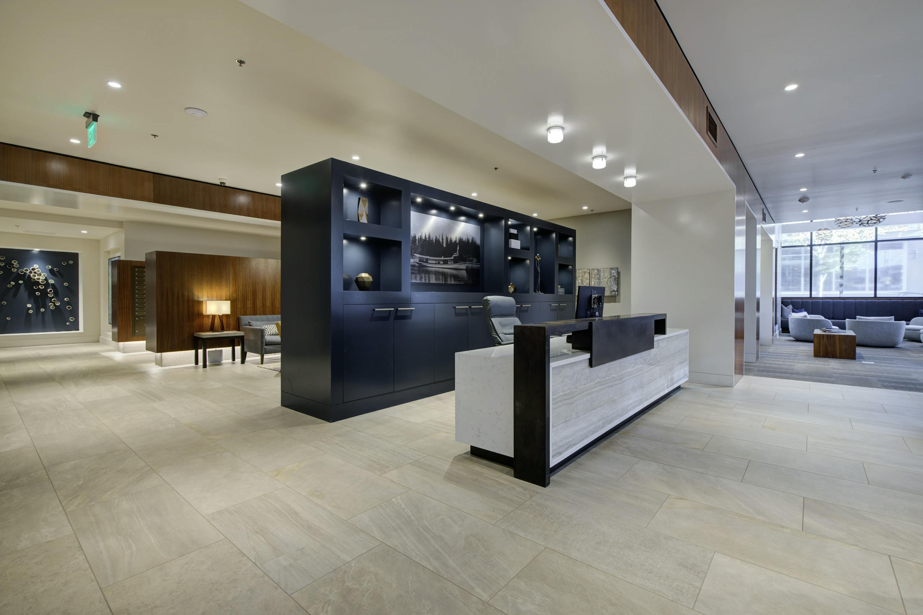 Open reception area at AMLI Waterfront apartments with navy shelving, wood and marble desk, and lounge seating in the background.