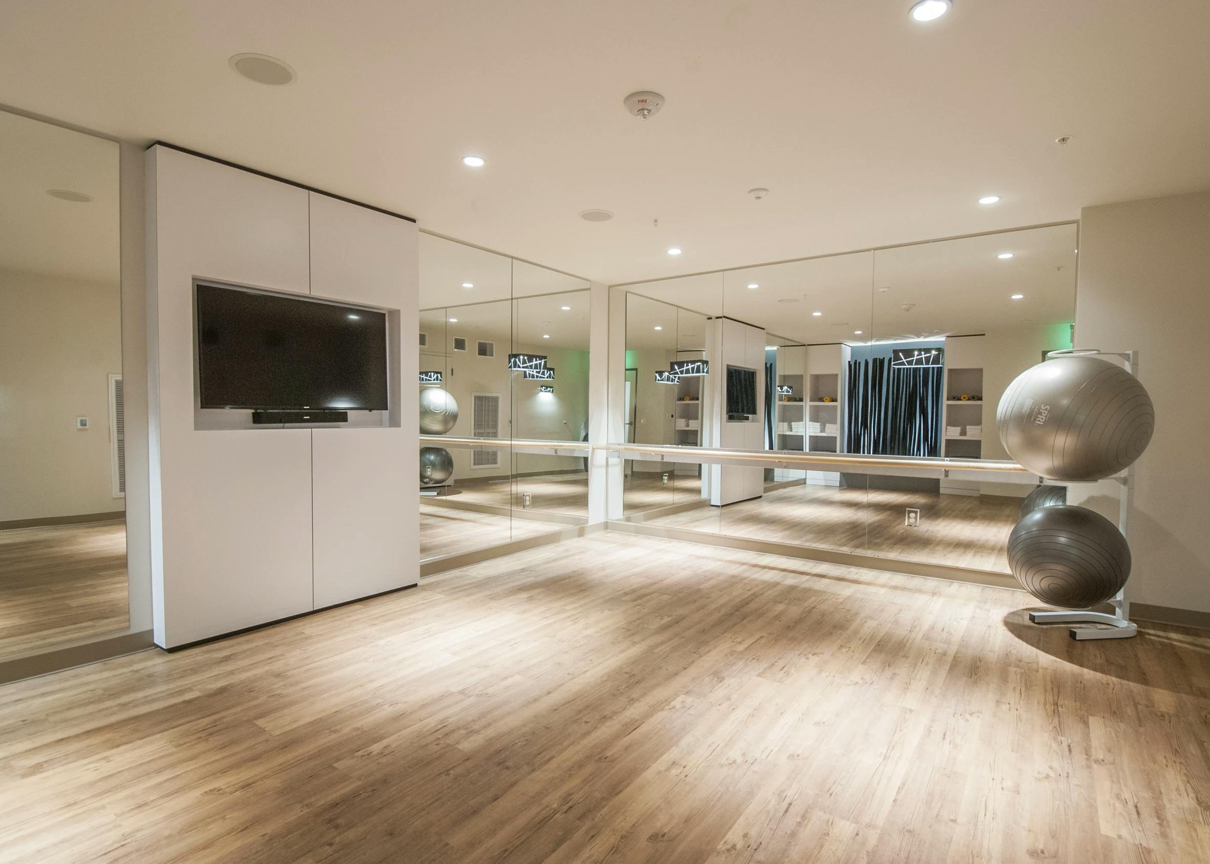 Yoga studio with mirrored walls, ballet bar, wood floors, mounted TV, and exercise balls at AMLI Waterfront apartments.