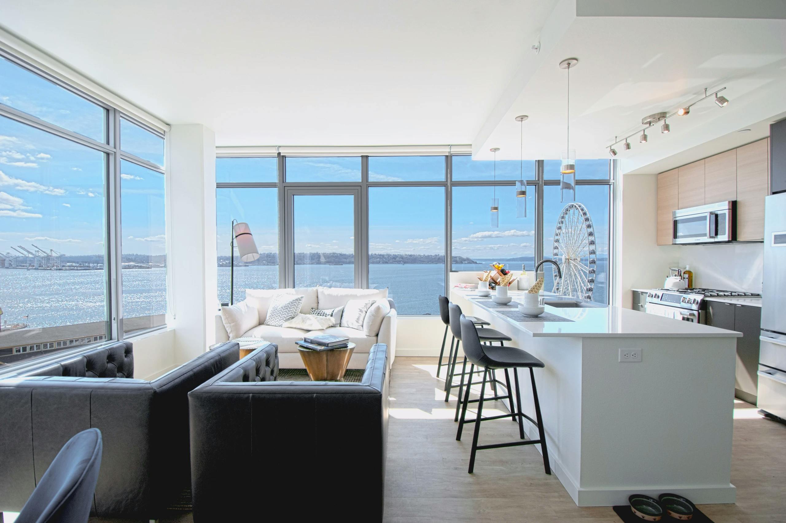 Corner living room at AMLI Waterfront apartments with white sofa, ferris wheel views, breakfast bar, and 2 walls of windows.